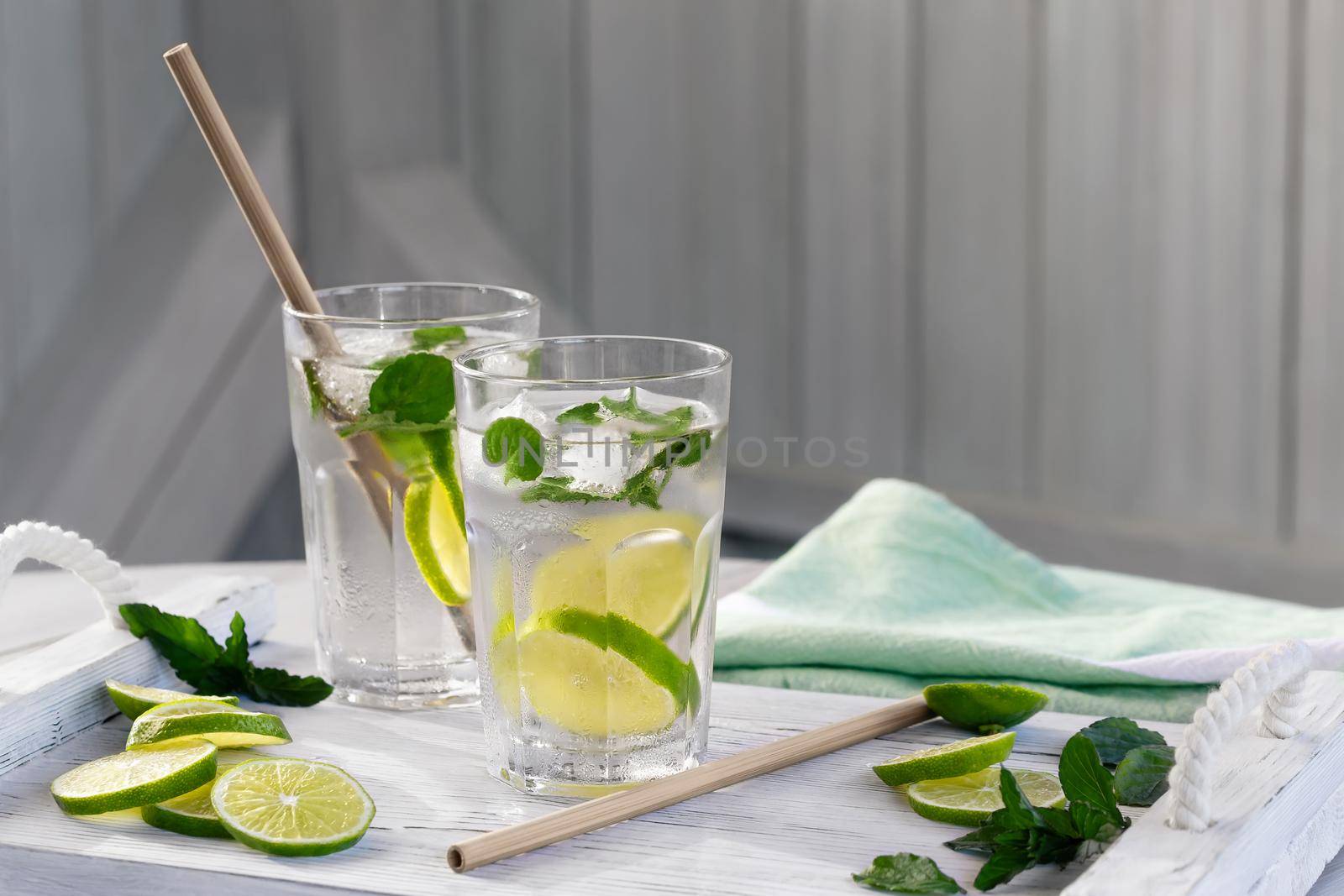 Summer refreshing mojito cocktails with lime and mint on a white wooden tray.