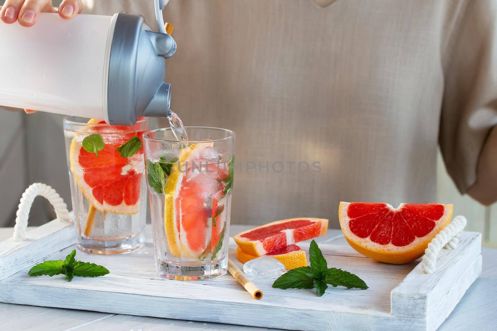Girl cooking summer refreshing fruit cocktail with grapefruit slices and mint by galsand