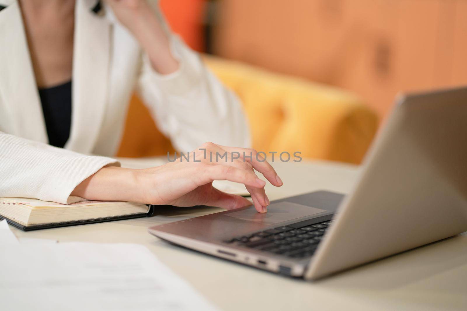 On face visible business woman in white jacket or suit at the desk working on laptop and making notes. Model female posing in business suit in the office. Business concept.