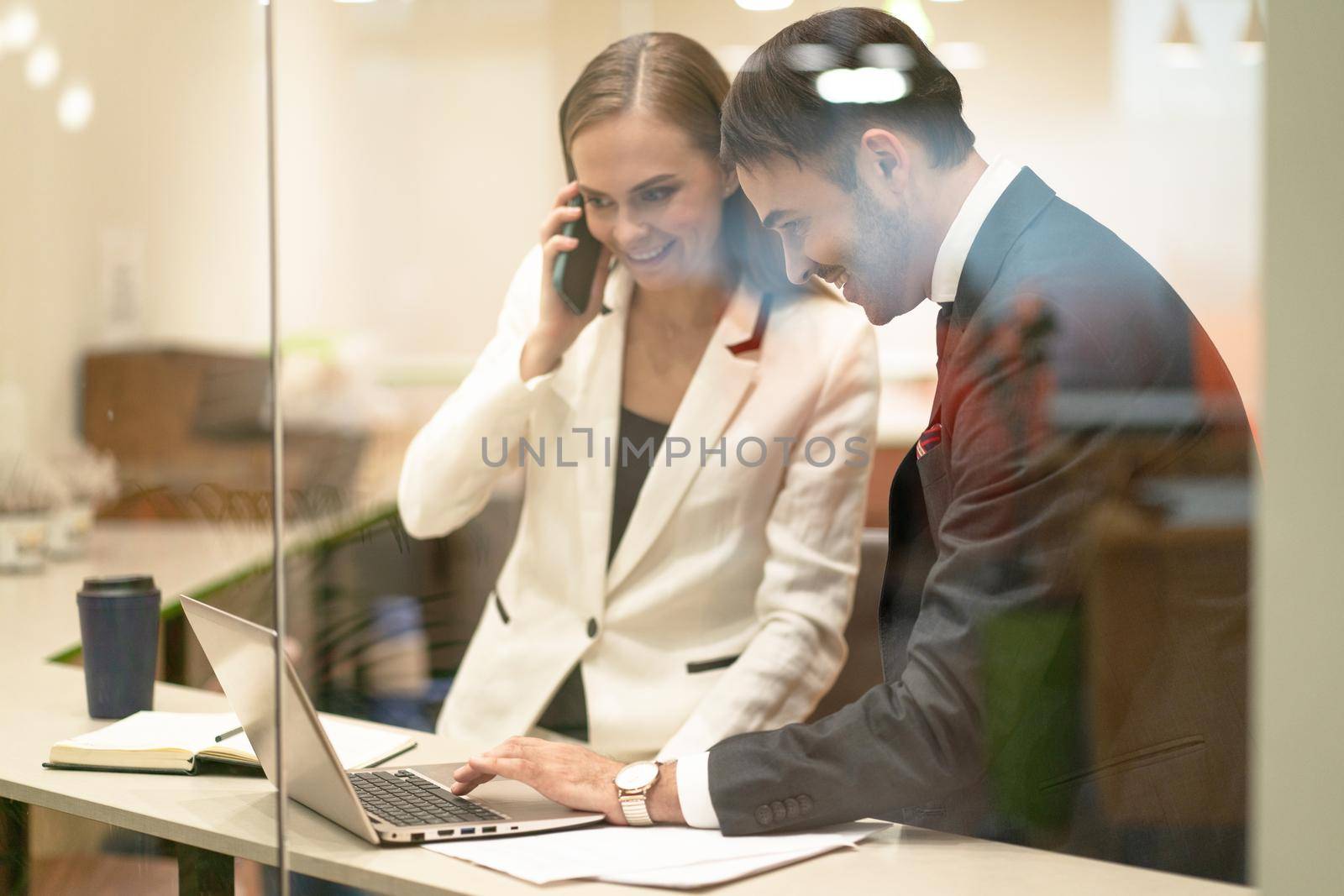 Business partners, stock brokers happy to see their successful buy or sell . Young business people in the suits with looking down at laptop standing behind the glass. Business concept.