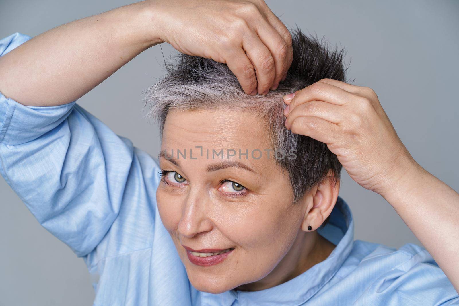 Pretty woman in 50s checking her hair or skull skin in mirror. Beautiful grey haired woman dealing with dandruff problem checking in mirror. Healthy hair and lifestyle concept by LipikStockMedia