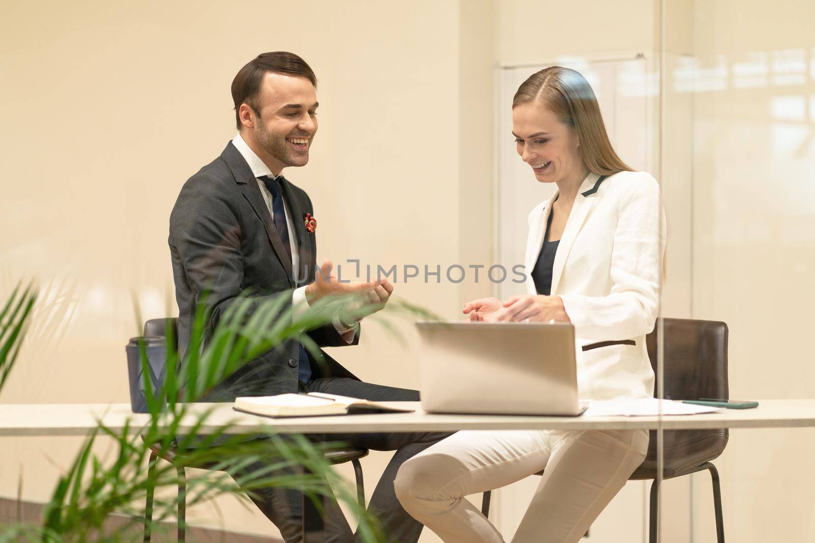 Two business partners discuss updates while having a coffee break. Young business people in the suits with coffee in hands looking down standing behind the glass.