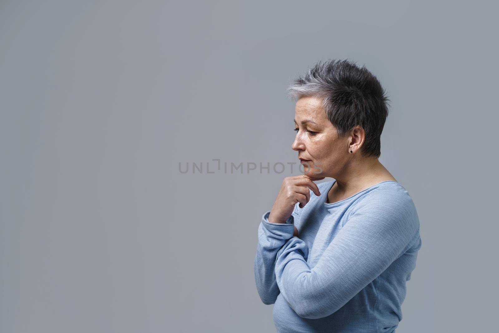 Portrait of thoughtful mature grey hair businesswoman posing with hands folded touching chin and copy space and place for product placement on left isolated on white background. Aged beauty concept.