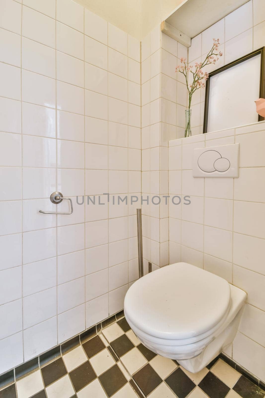 Interior of narrow restroom with sink and wall hung toilet with white walls and checkered floor