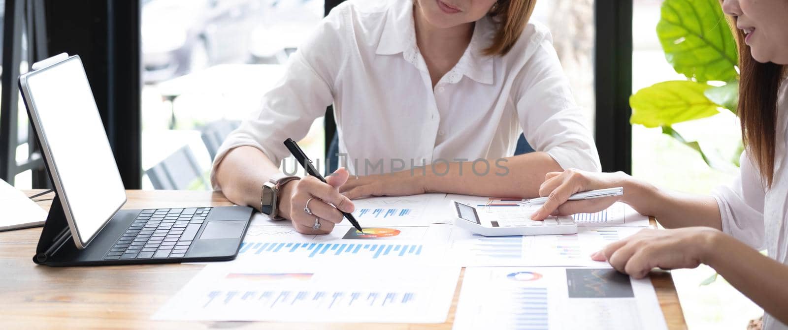 Two women analyzing documents while sitting on a table in office. Woman executives at work in office discussing some paperwork..