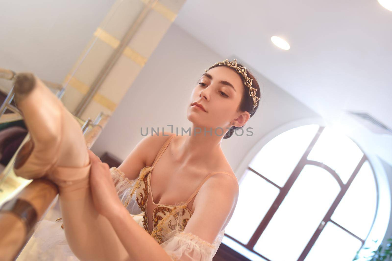 charming Ballerina stretches herself near barre and mirrors in the classroom