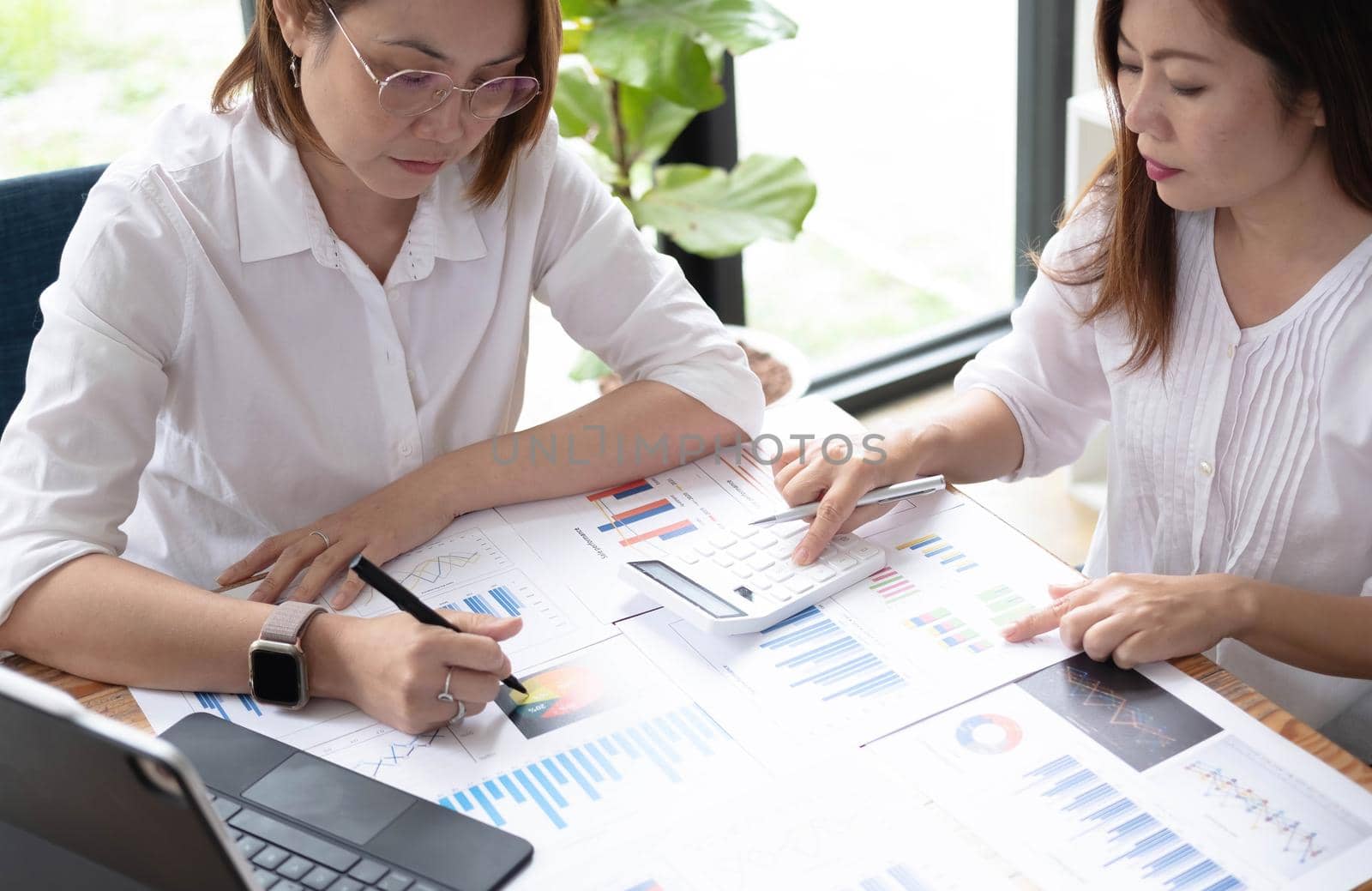 Two women analyzing documents while sitting on a table in office. Woman executives at work in office discussing some paperwork..