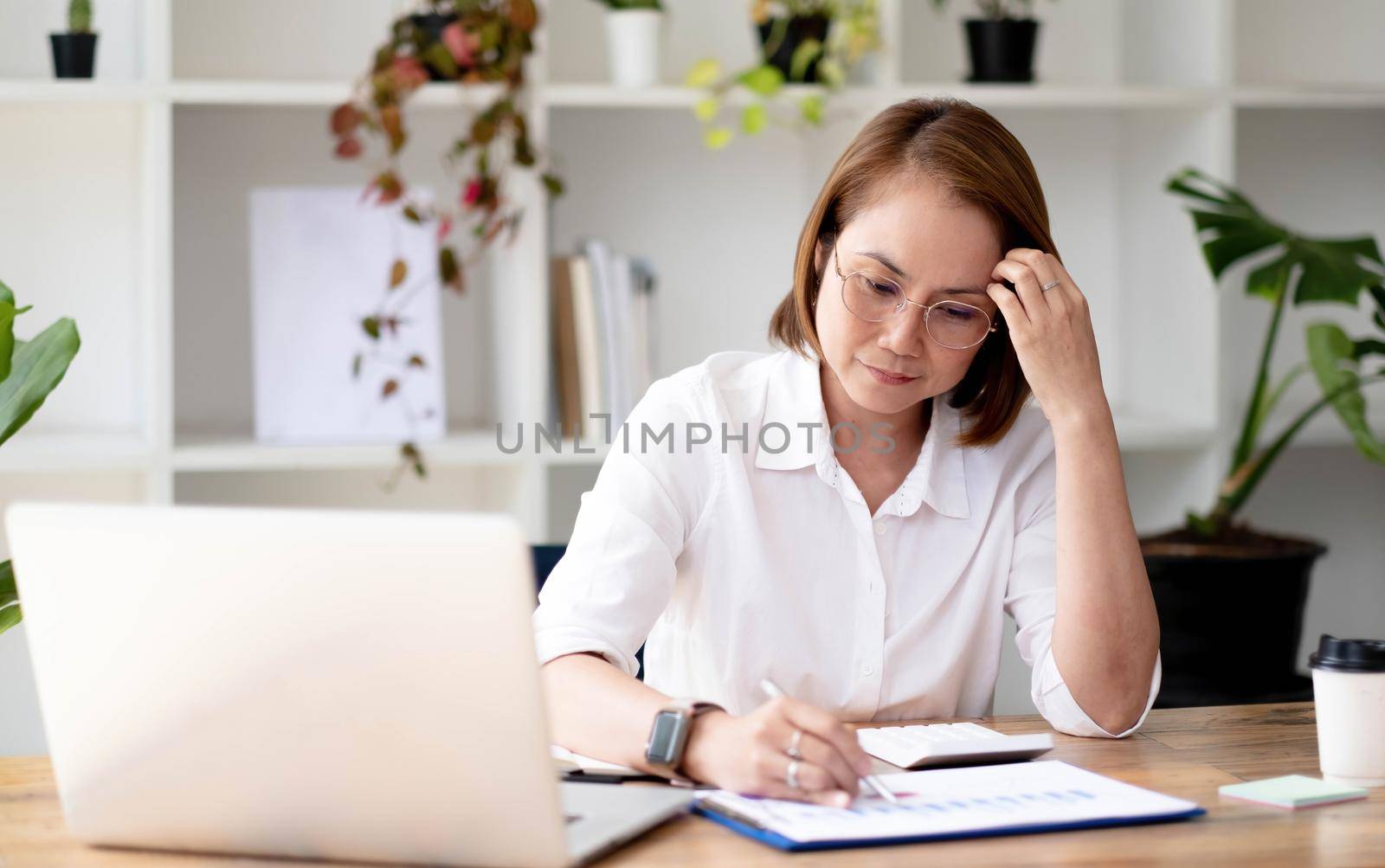 Asian aged-female senior college teacher in glasses reviewing and examining her college student's report in her modern house..