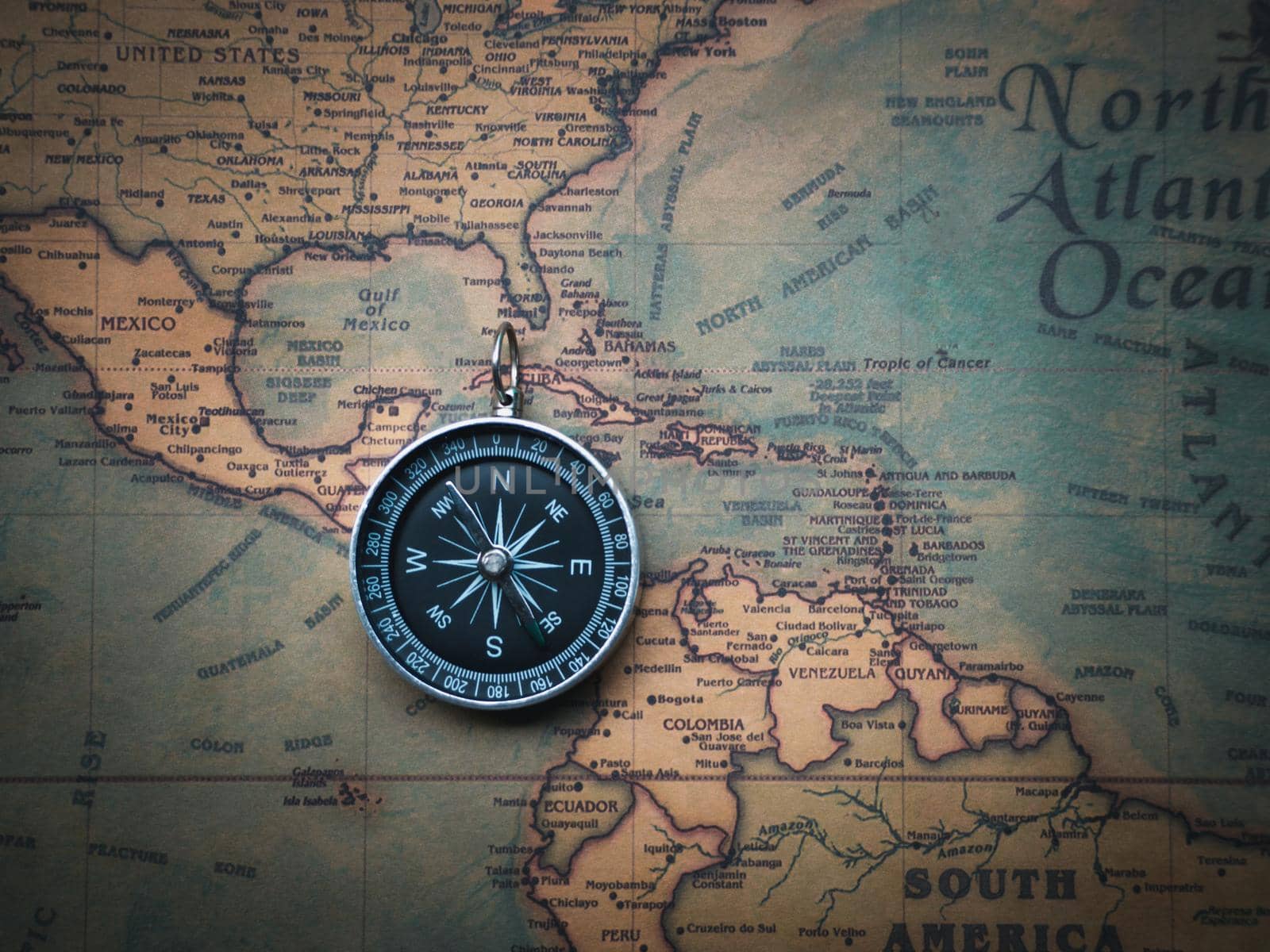 The compass is placed on the ancient or vintage world map between the United States of America and South America. Travel geography navigation concept background. by Chakreeyarut