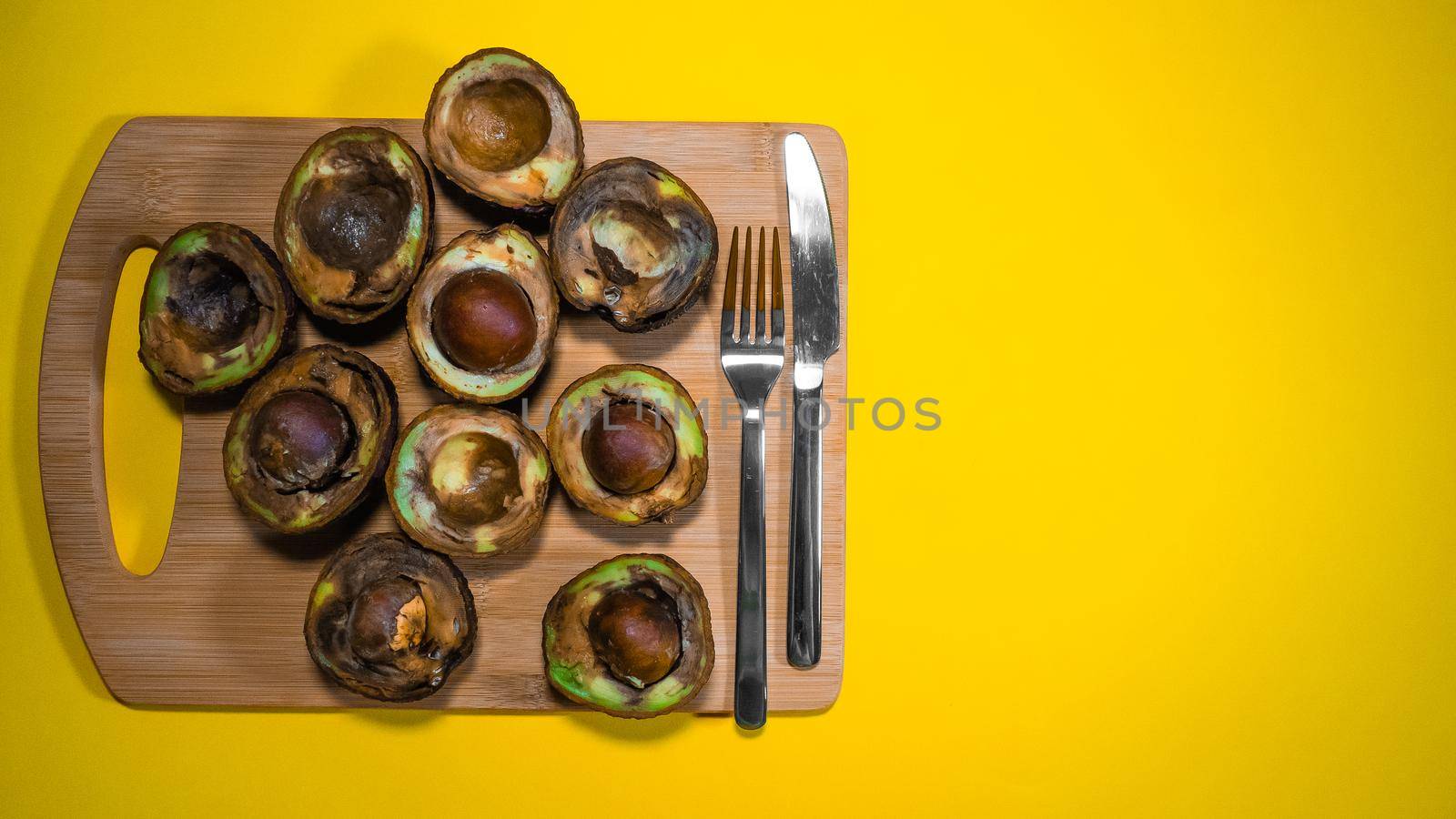 Overripe Fruits Concept on Yellow background. Bad Vegan food. Rotten Avocado on wood Chipper. Copy space Necomestibile Food. Stop wasting food. Bad Avocado Halfs cannot be eaten.