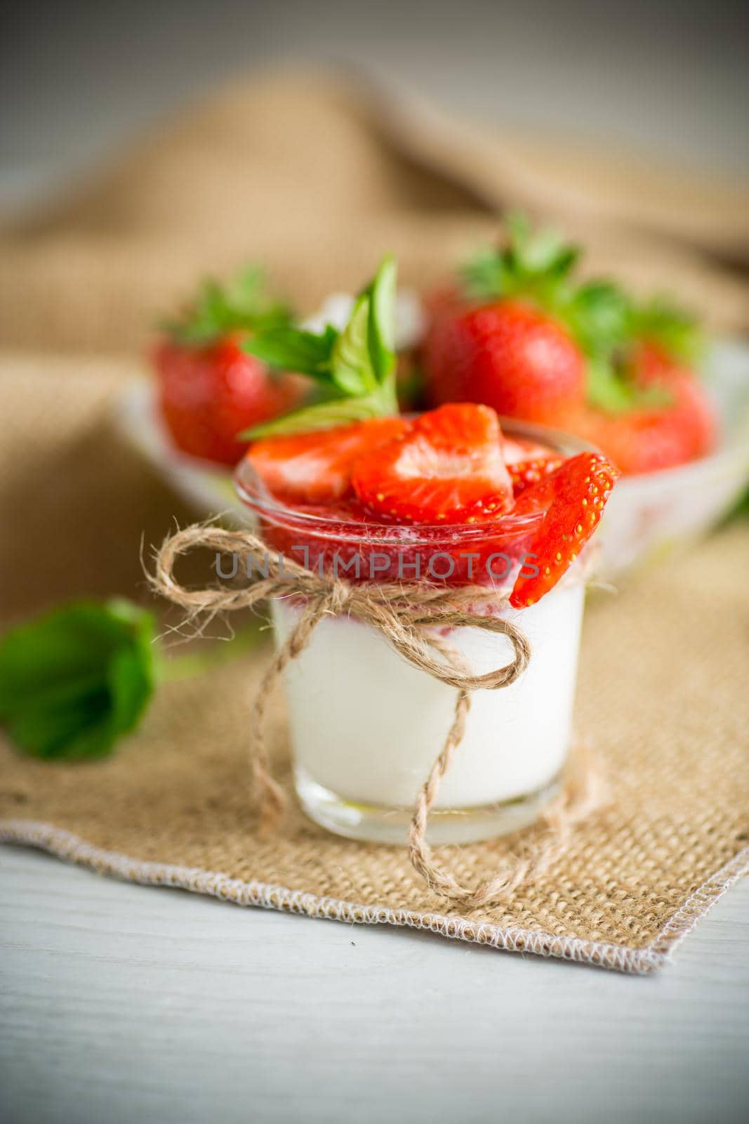 sweet homemade yogurt with strawberry jam and fresh strawberries in a glass cup, on a wooden table.