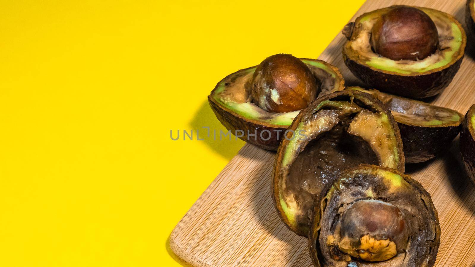 Rotten Avocado on Yellow background. Close up details Rotten tropical Fruits on bambus Chipper. Copy space. Yellow background contains Unhealthy Food.