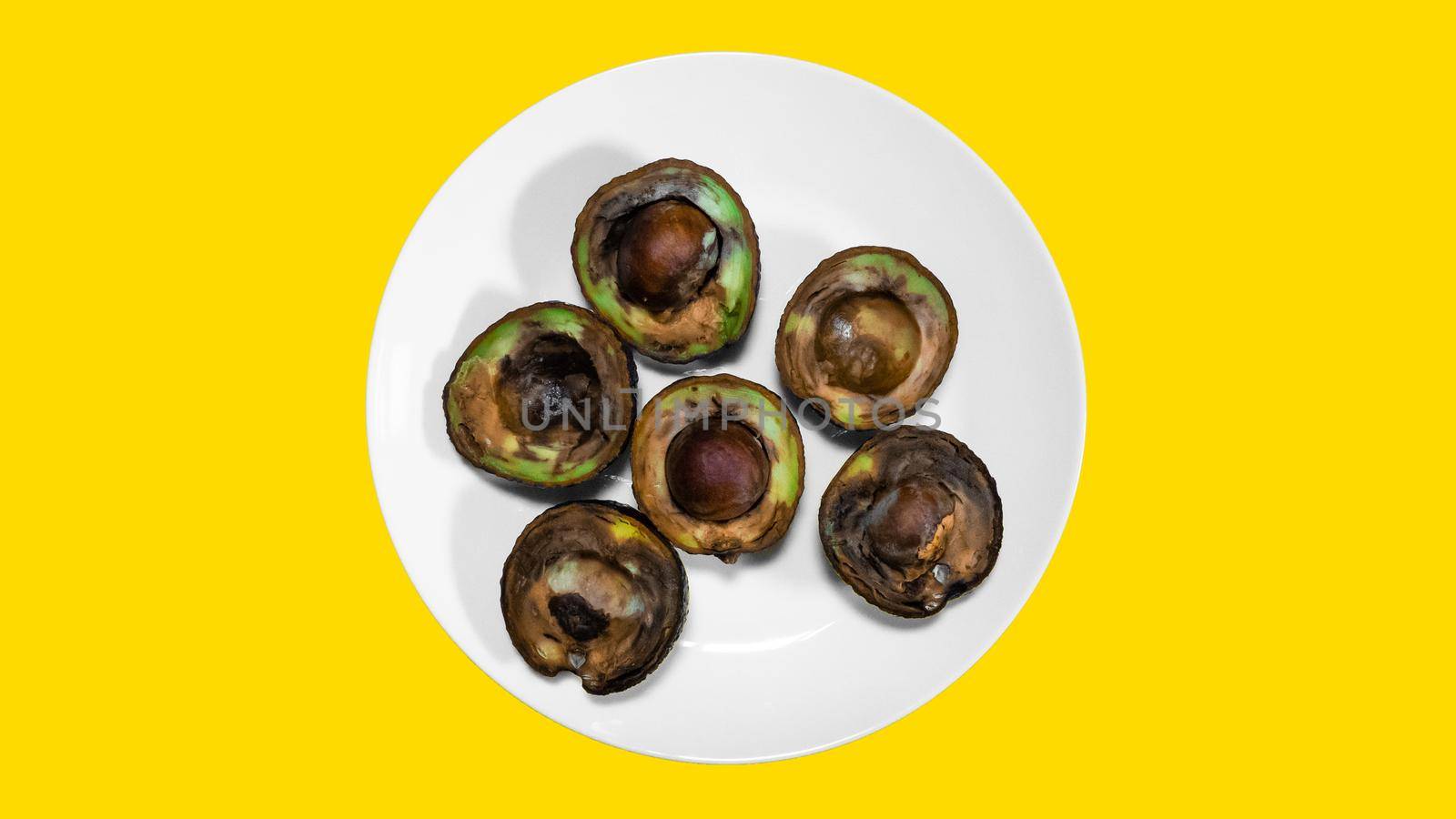 Ugly food on yellow background. Rotten tropical Avocado fruits. Concept of rotten fruit. Avocado on a plate.