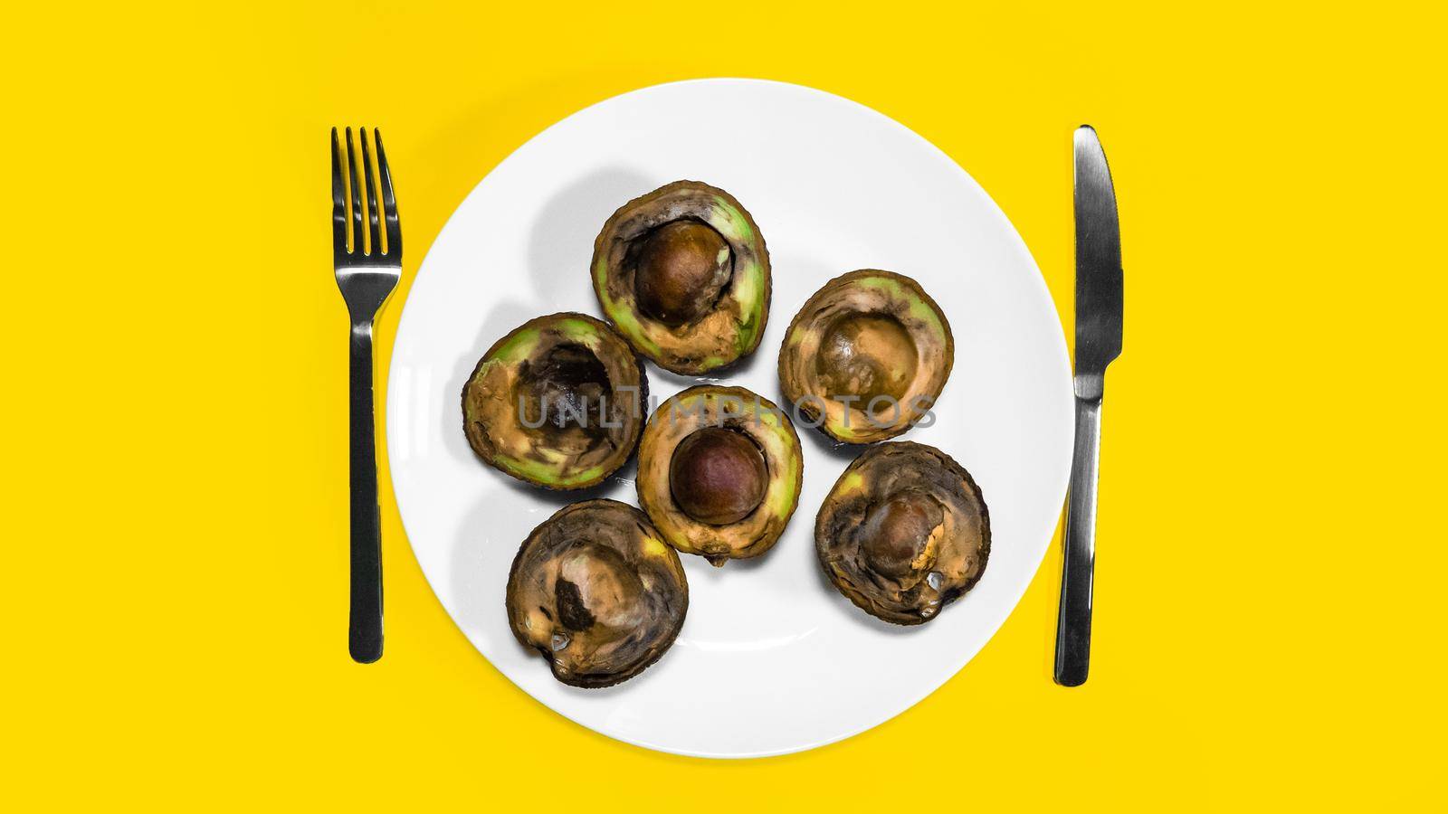 Bad Avocado halfs placed on plate with fork and knife Yellow background. by RecCameraStock