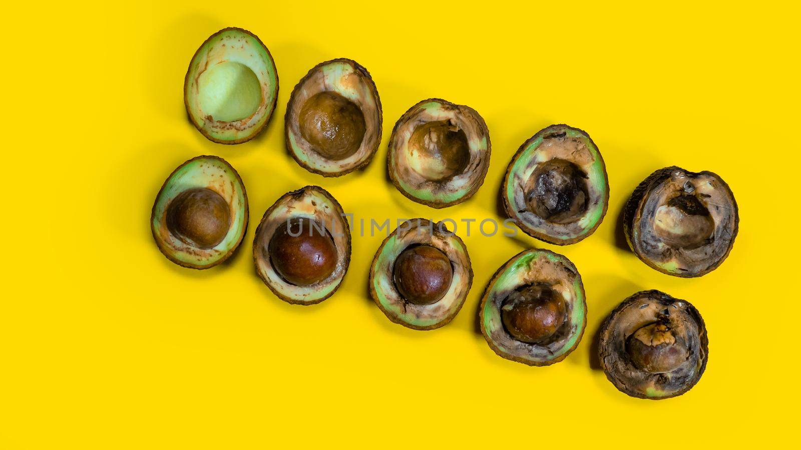 Avocado evolution from good to rotten fruits. Creative composition many avocado cuts in halfs on yellow background. Rotten avocado piles cannot be eaten.