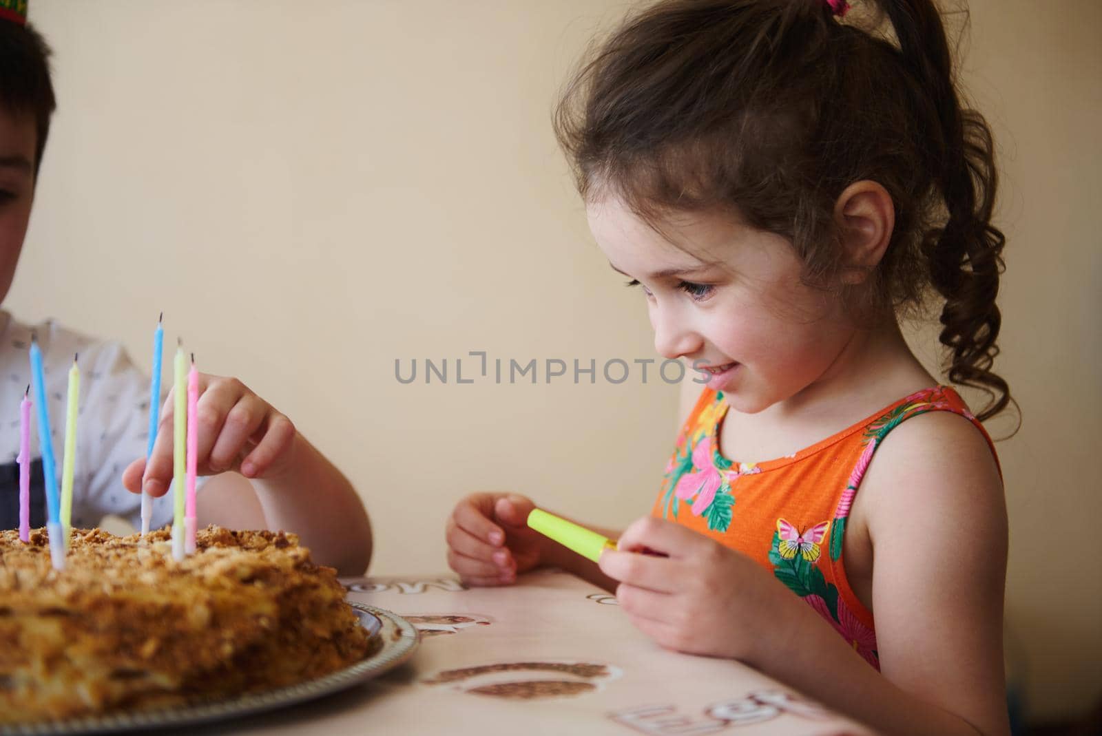 Close up portrait of a happy smiling adorable child, 5 year old Caucasian girl standing at the table with a birthday cake. Celebration, anniversary event concept
