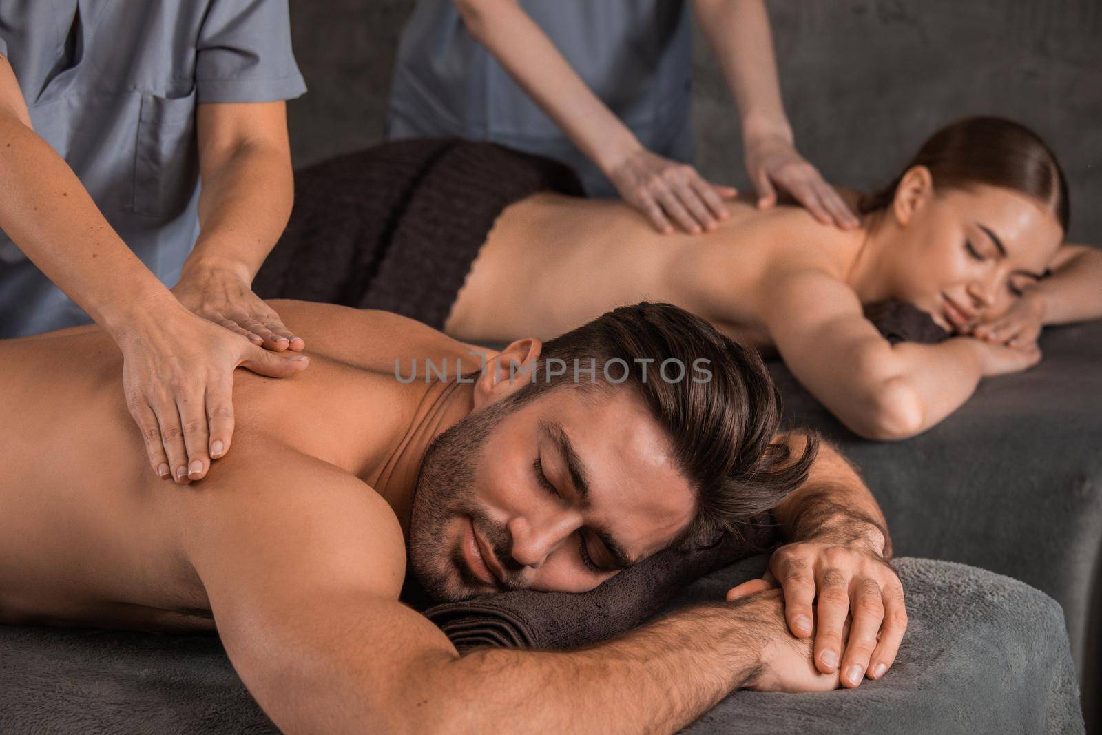 Happy young couple enjoying spa procedures, back massage