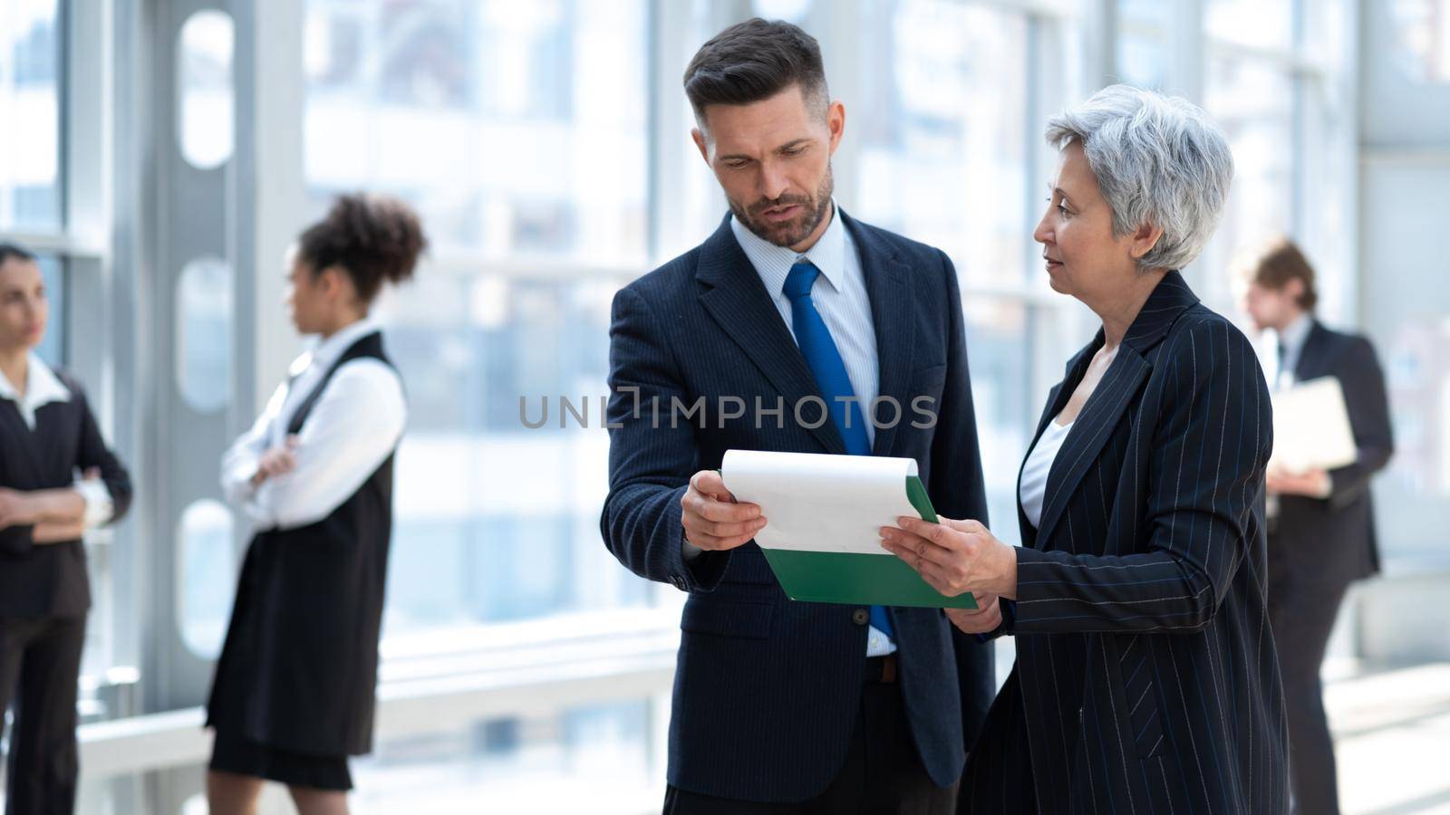 Meeting of group of business people in the office standing in front of a large window working with documents