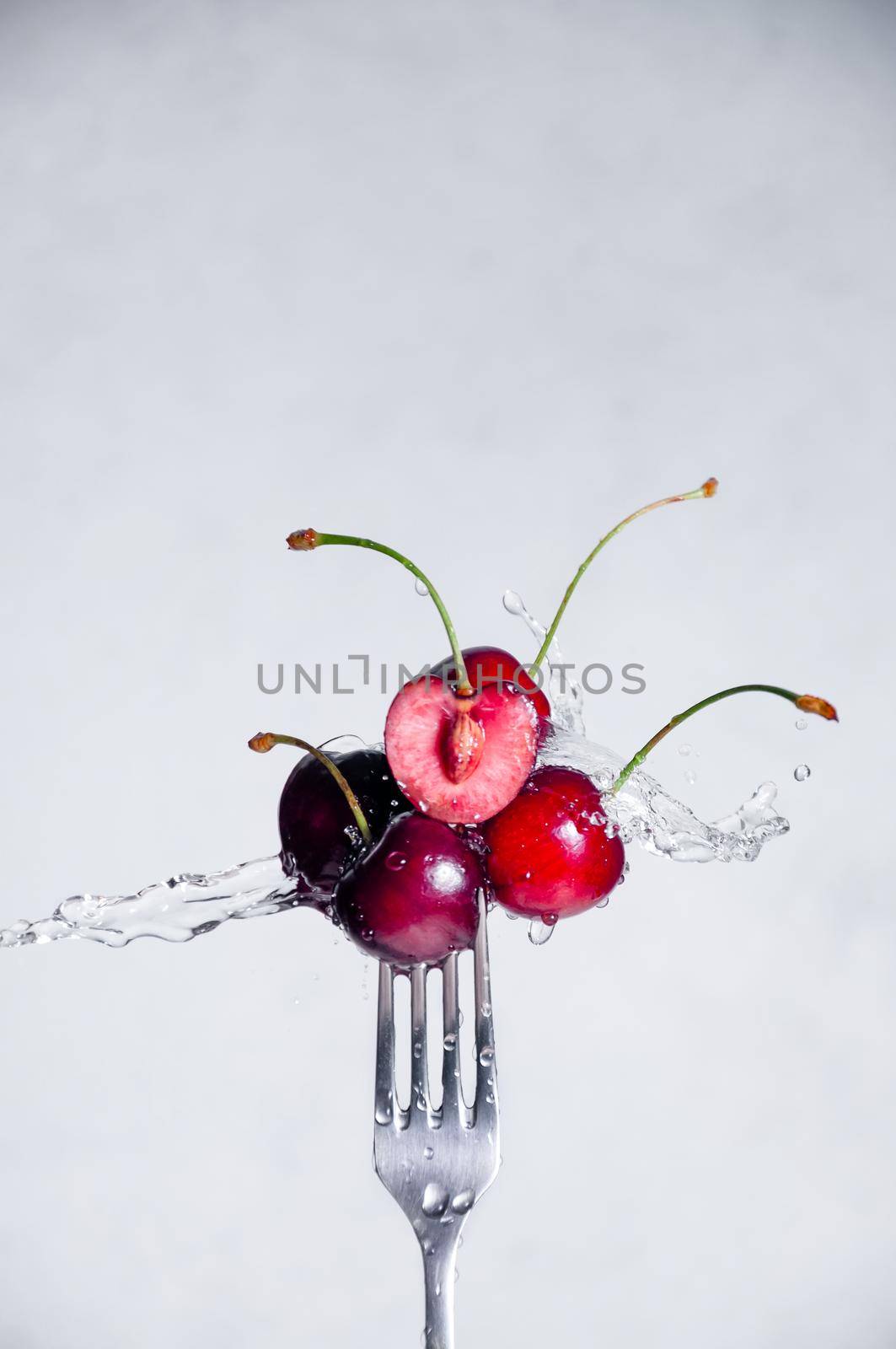 Close up Composition of Cherries on Fork Flying in the air with Water Splashes on the Light Grey Background by Svetlana_Belozerova