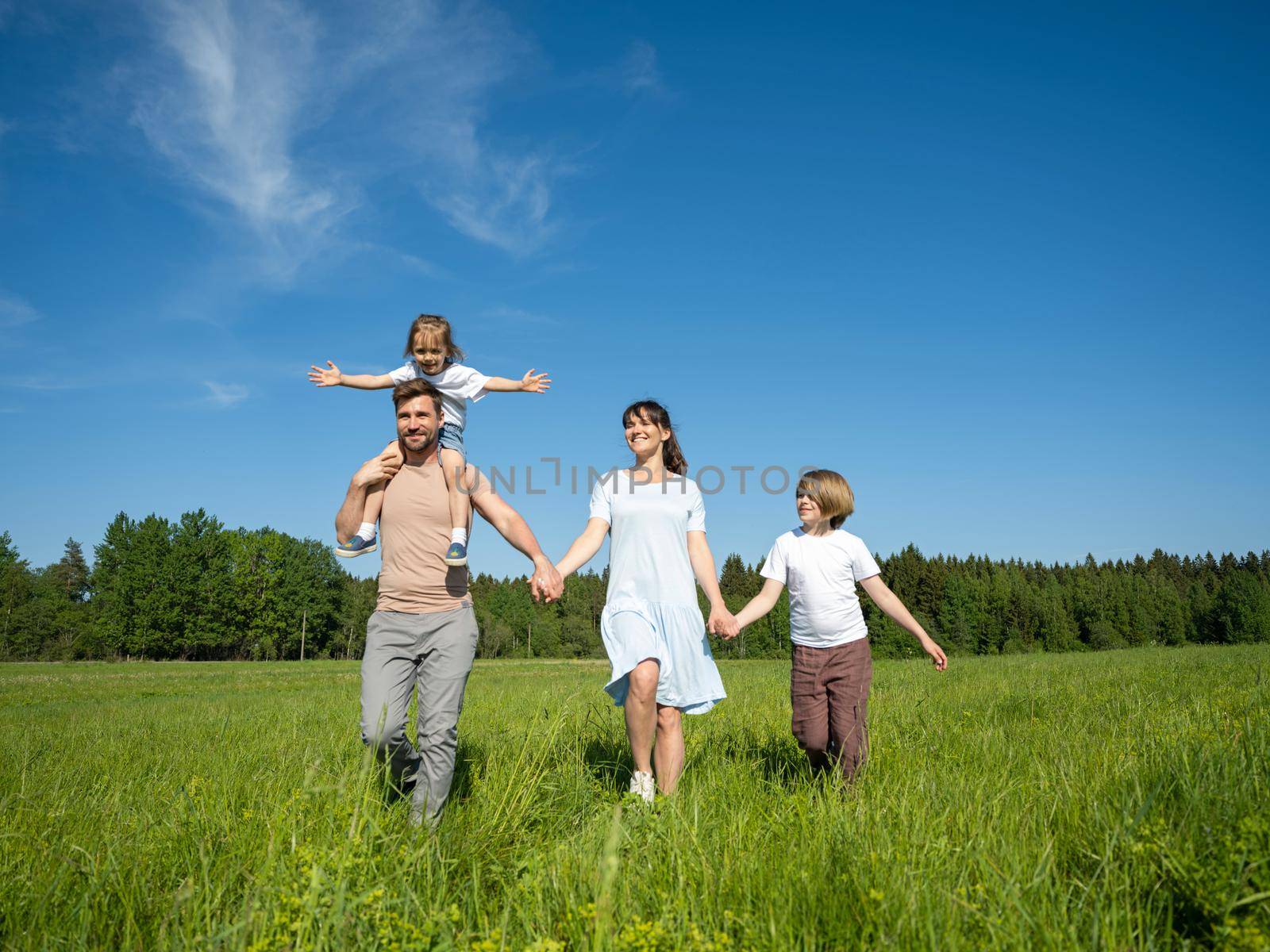 Happy family of parents and two children walking on summer grass meadow