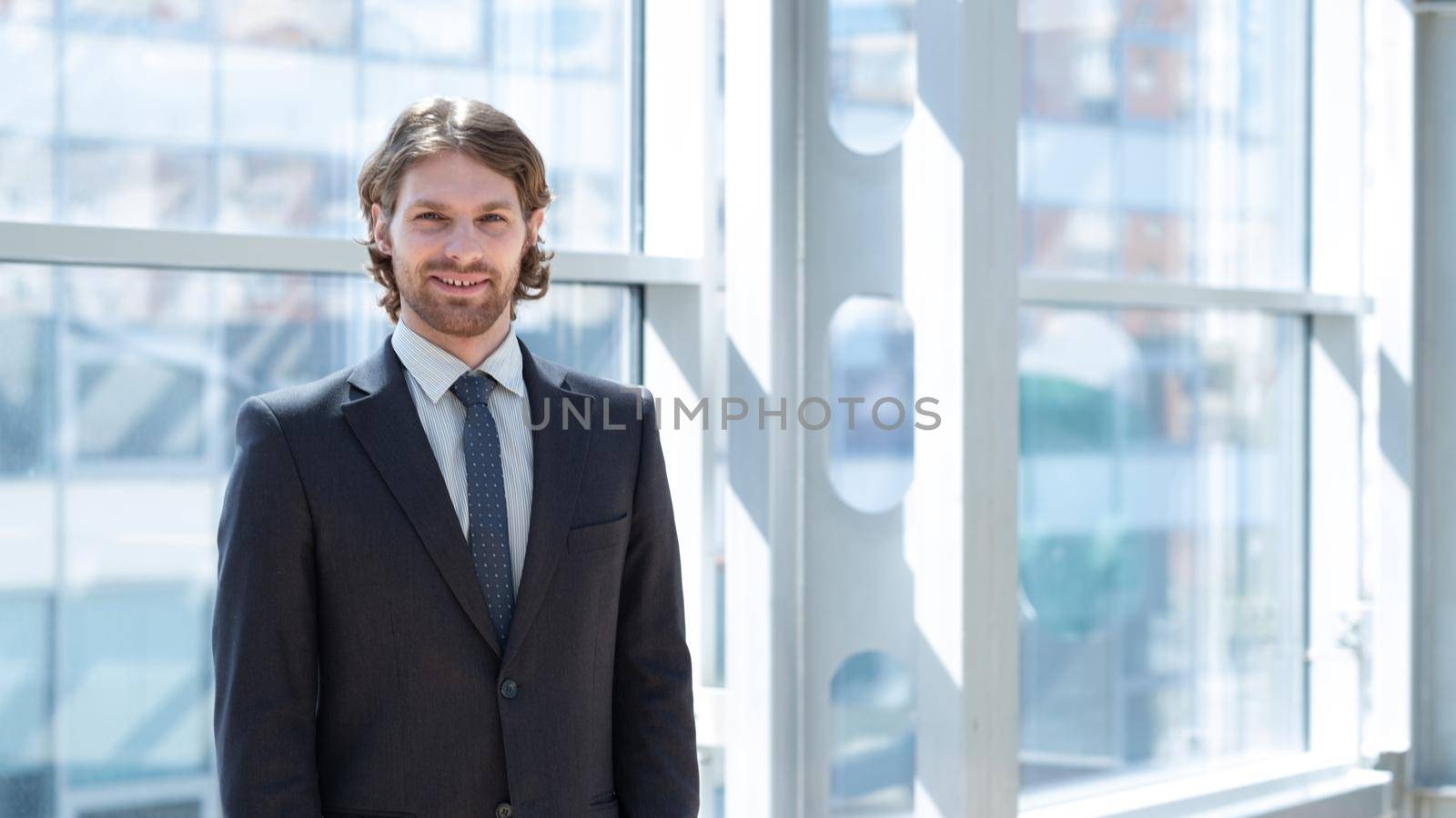 Smiling young businessman in suit standing in front of window in office