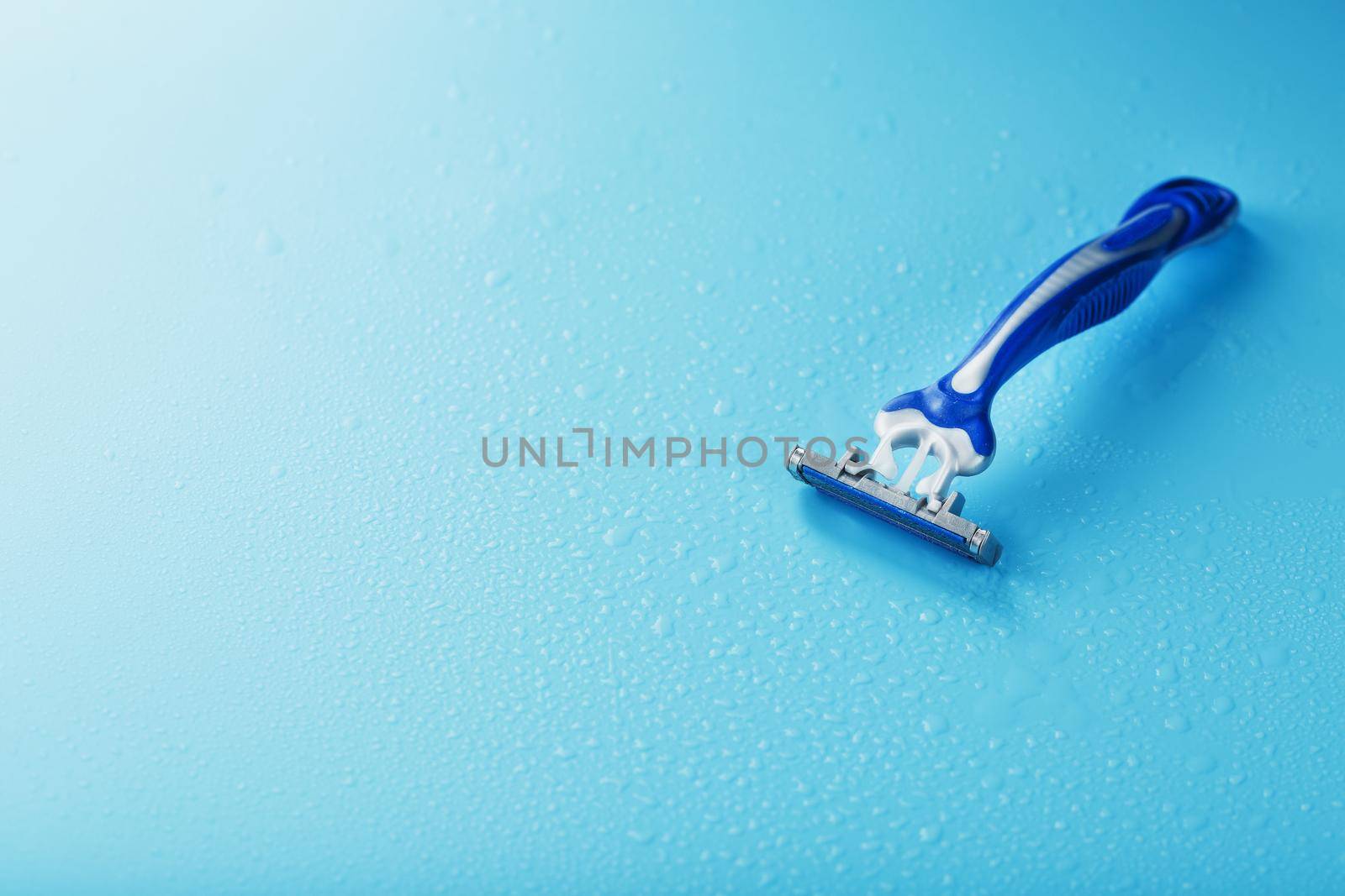 Razor blades on a blue background with drops of icy water by AlexGrec