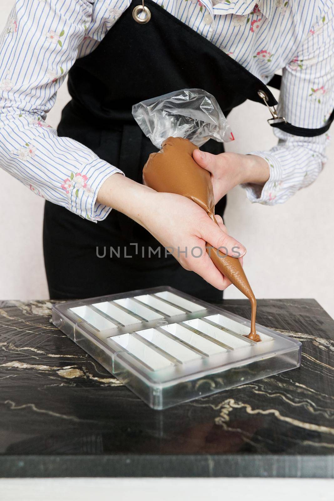 Chocolatier pours chocolate into molds. Chef using pastry bag filling hot melt chocolate into mold. Concept for making homemade chocolate dessert