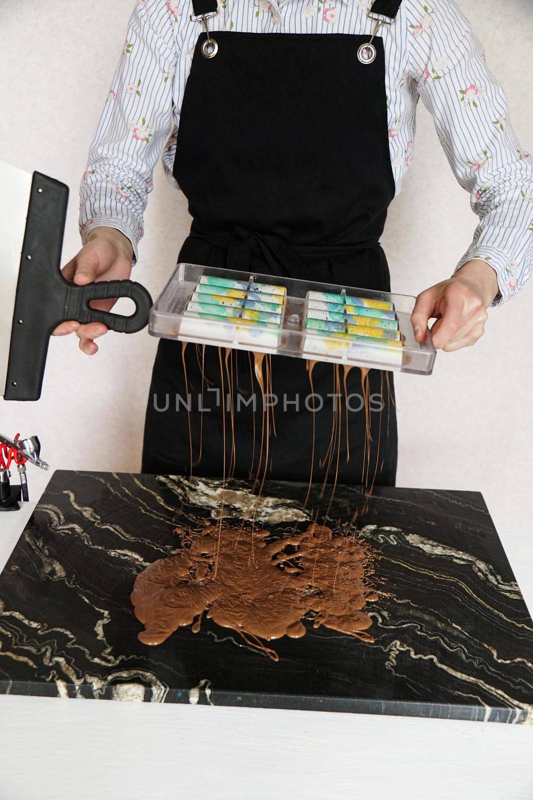 Woman chocolatier makes chocolate in the kitchen. She pours the rest of the hot chocolate out of the plastic mold.