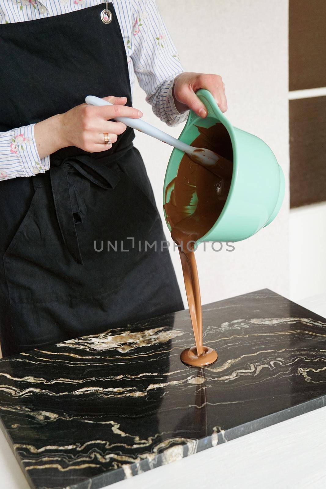 Closeup photo - woman stirs chocolate and pours on a stone board for making homemade chocolates. Candy making, pastry production, dessert concept