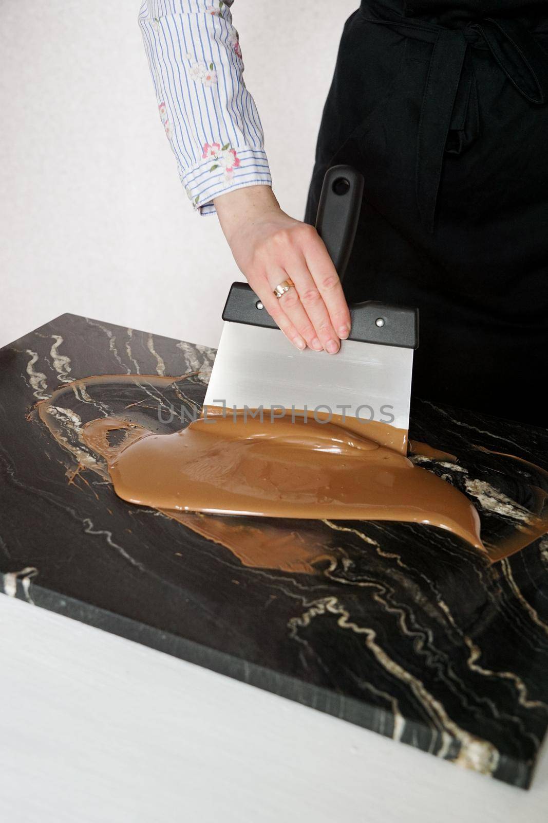 Male chocolatier uses a spatula to stir the tempered liquid chocolate on a granite table