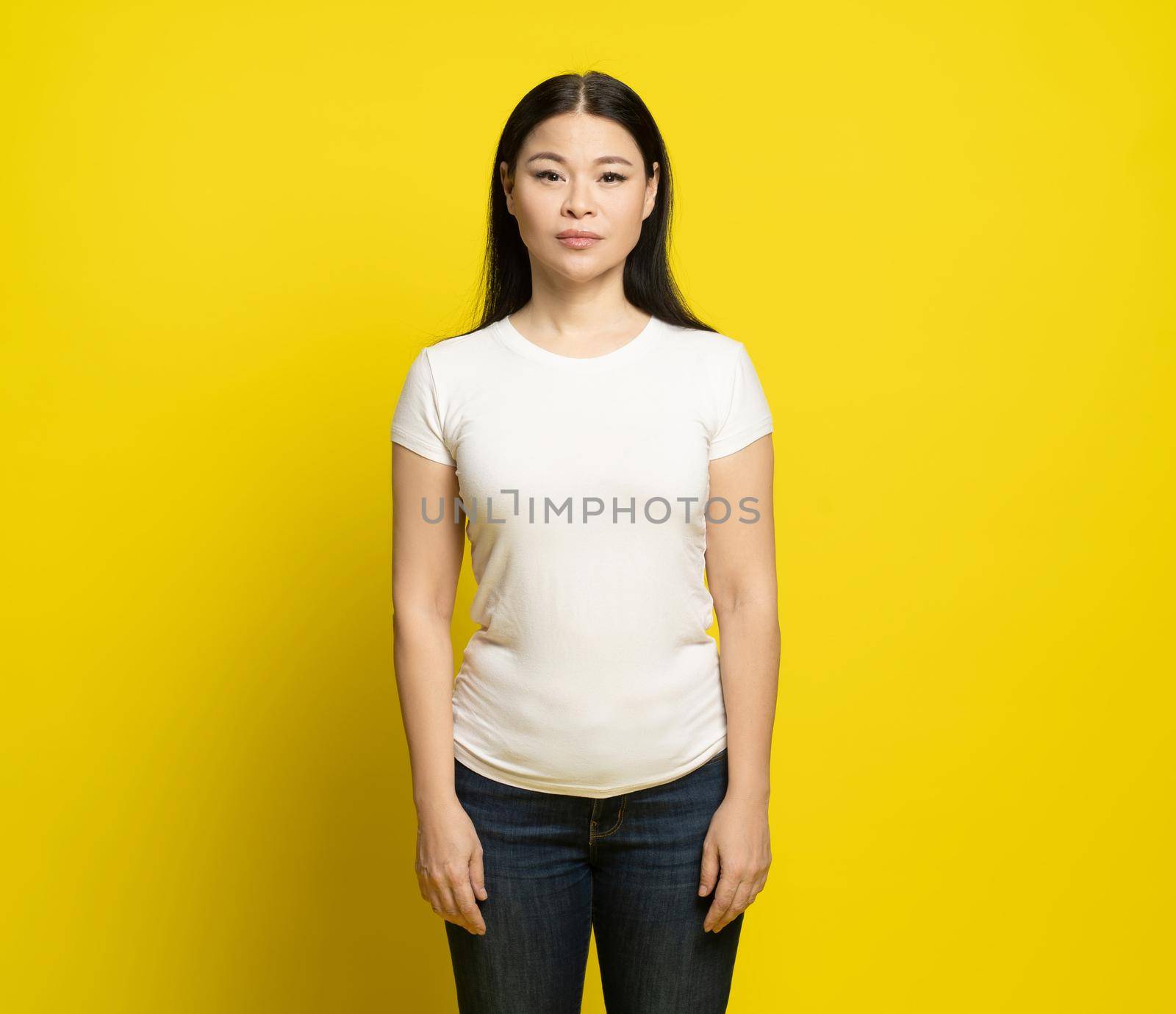 Sad asian woman with long hair wearing white t-shirt and jeans standing happy laughing isolated on yellow background. Fashion concept by LipikStockMedia