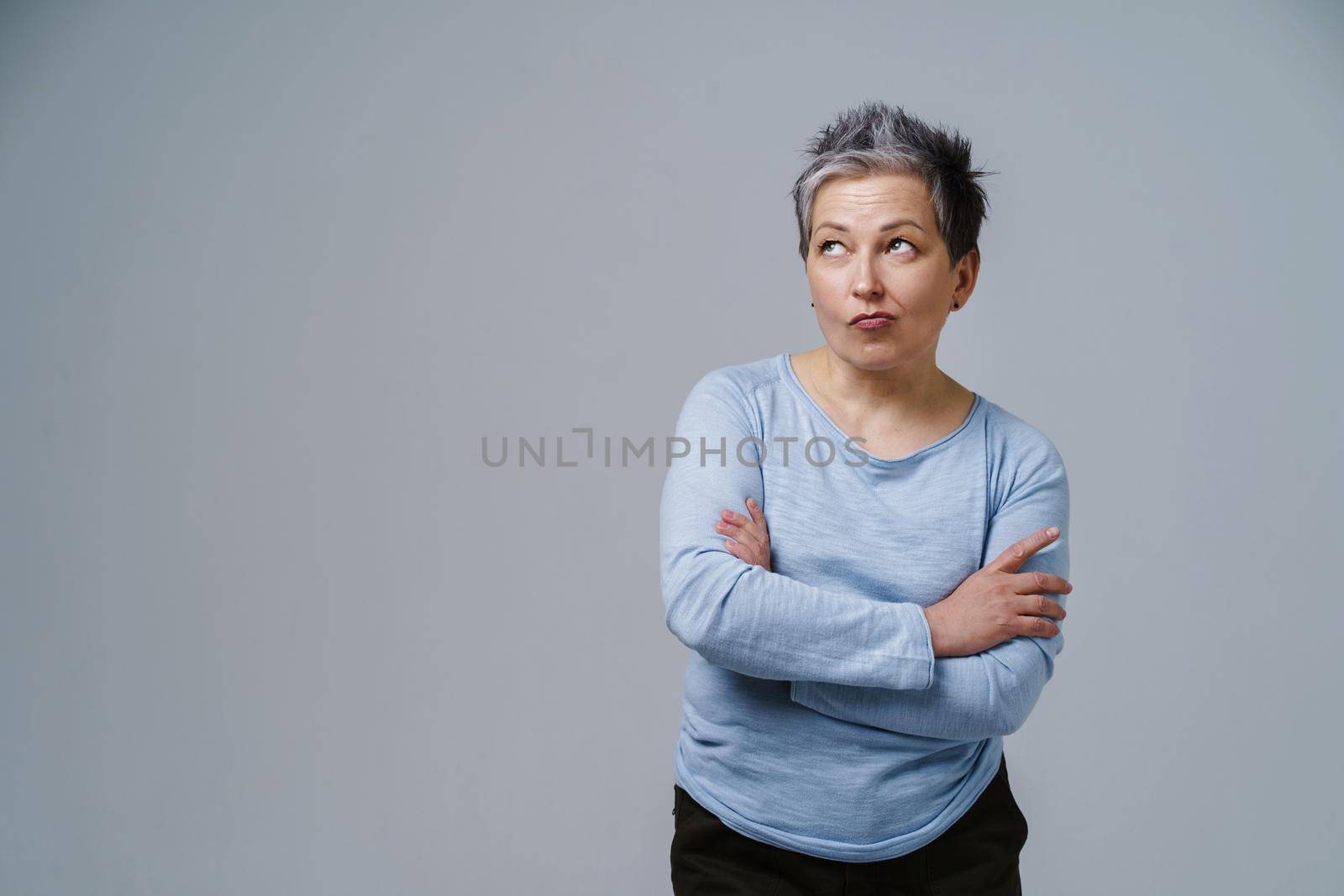 Pensive, thoughtful, doubt mature woman with grey hair in 50s posing with hands folded and copy space on left isolated on white background. Place for product placement. Aged beauty. Toned image.