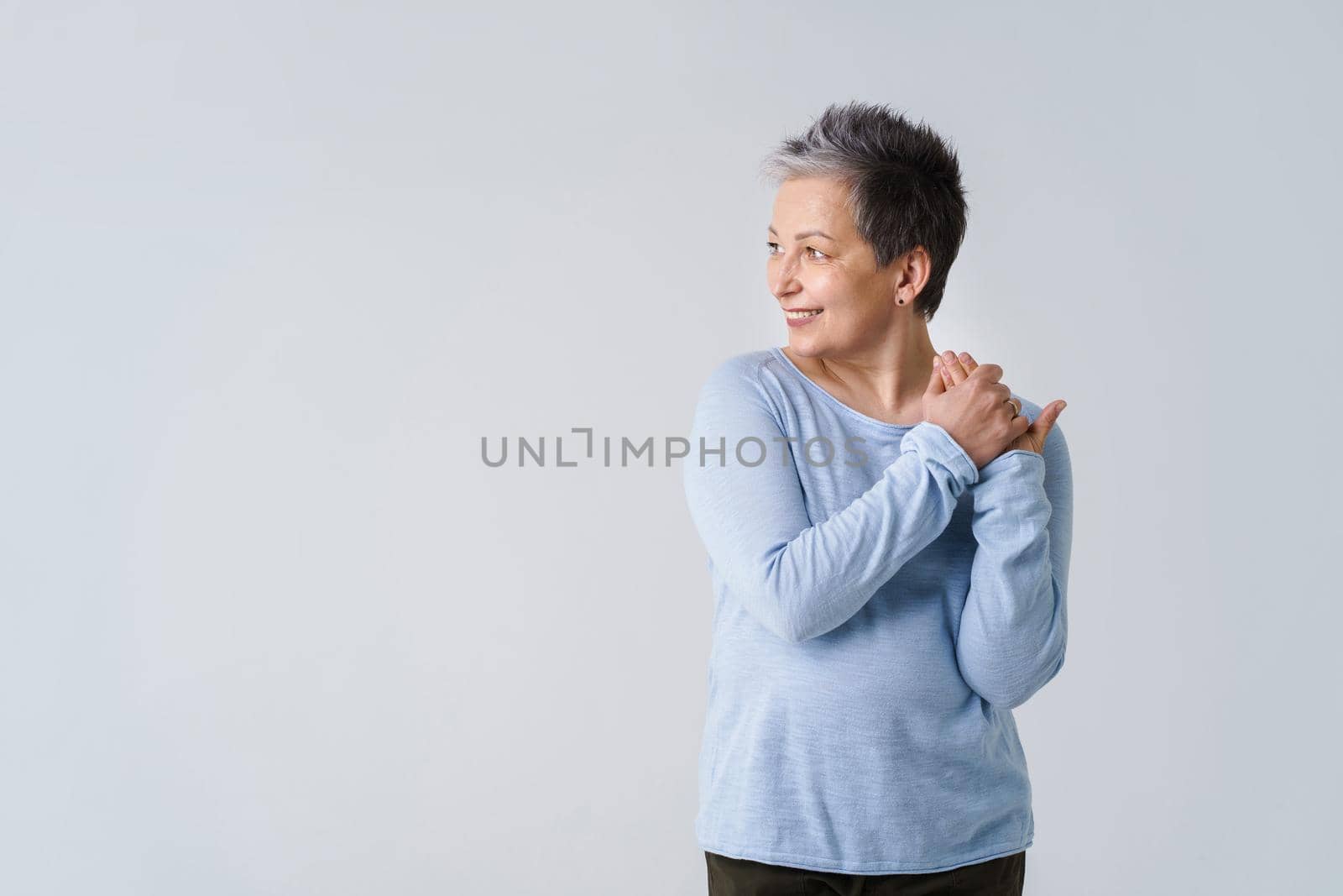 Beautiful mature grey hair european woman in 50s posing looking sideways with hands folded and copy space isolated on white. Stylish elderly senior businesswoman executive, portrait by LipikStockMedia