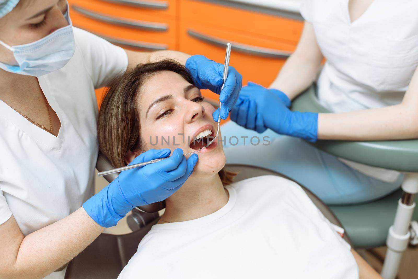 Medical treatment at the dentist office. Female dentist and assistant in dental office examining young woman with tools in dental clinic by etonastenka