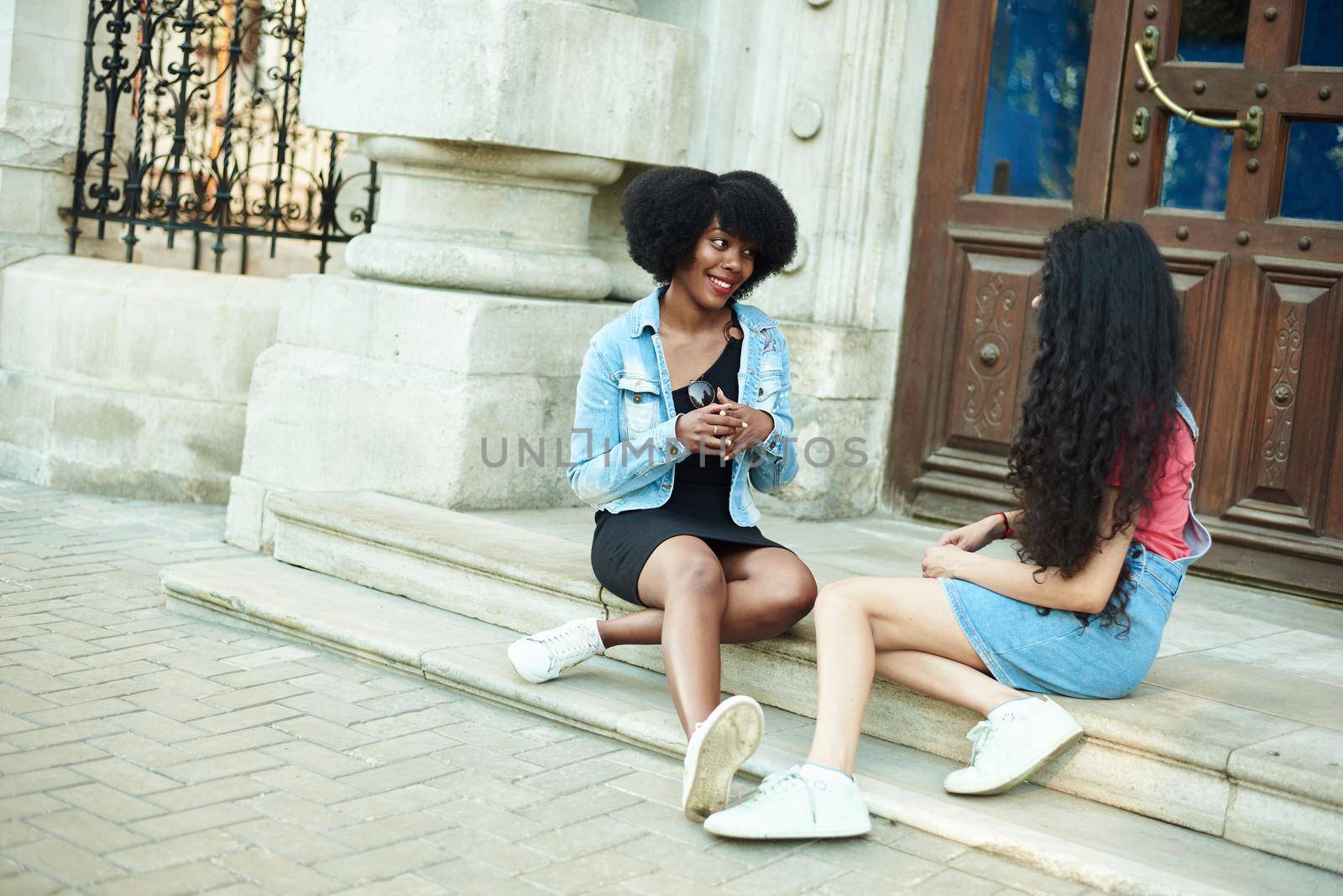 An African American woman communicates with her friend. sitting on the stairs of the campus. Students are discussing classes at the university by etonastenka