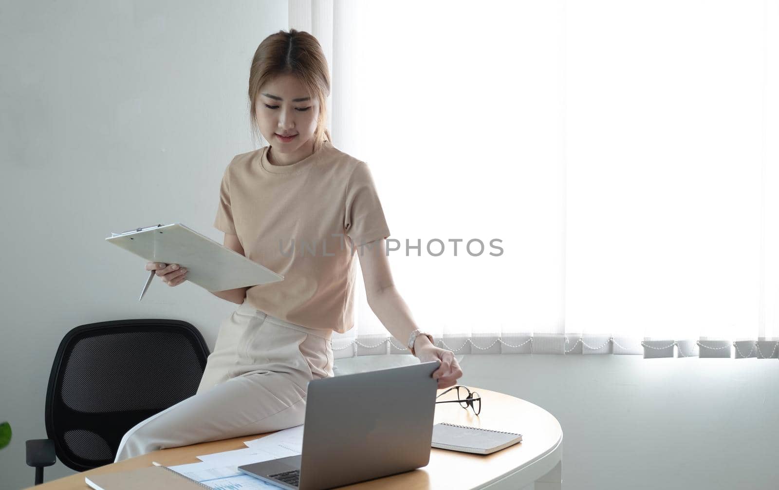 Smiling beautiful young asian woman working on laptop computer while sitting at the cafe indoors, looking through documents by wichayada