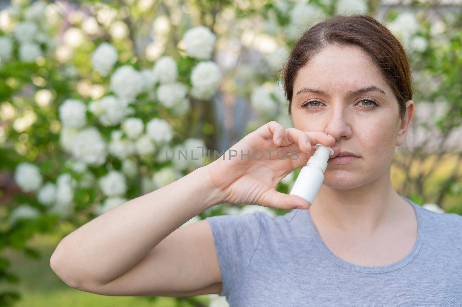 Caucasian woman uses a nasal spray while walking in the park. by mrwed54