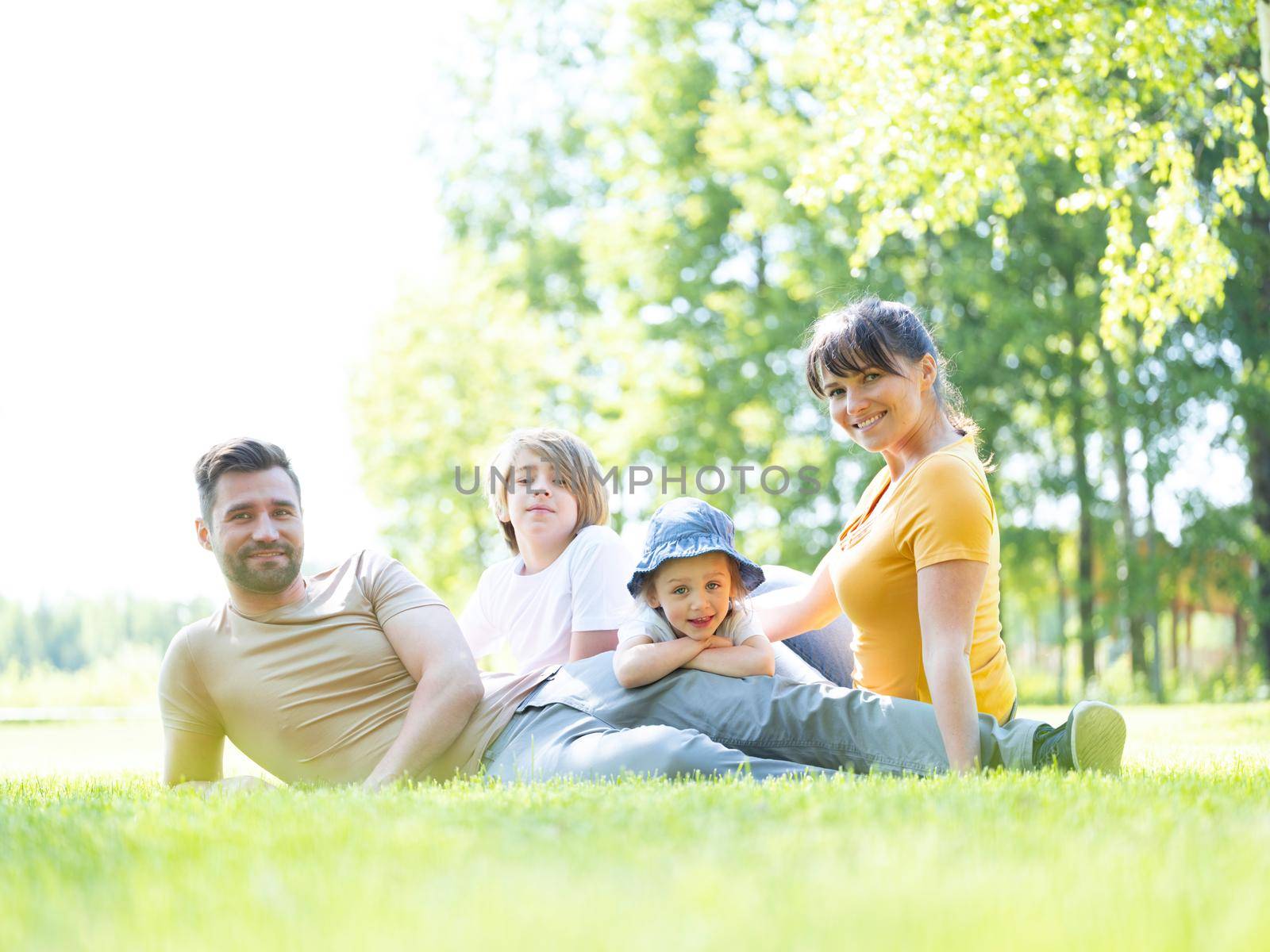 Caucasian family of parents and children sitting together in park, weekend summer vacations.