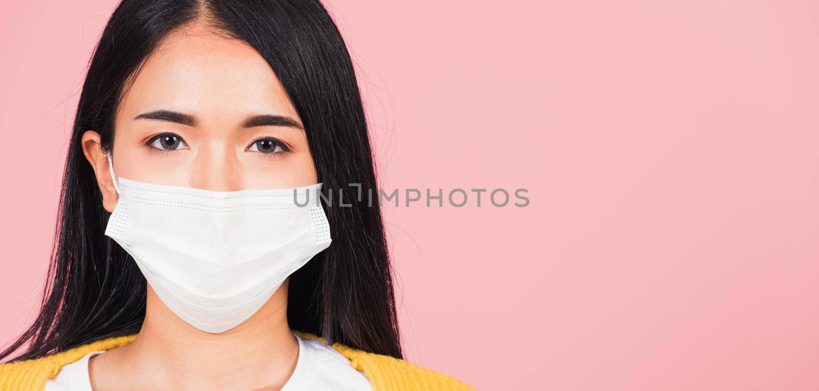Closeup face Asian beautiful young woman wearing medical mask protection against germs for prevent infection coronavirus, COVID-19, studio shot isolated on pink background, medical health care concept