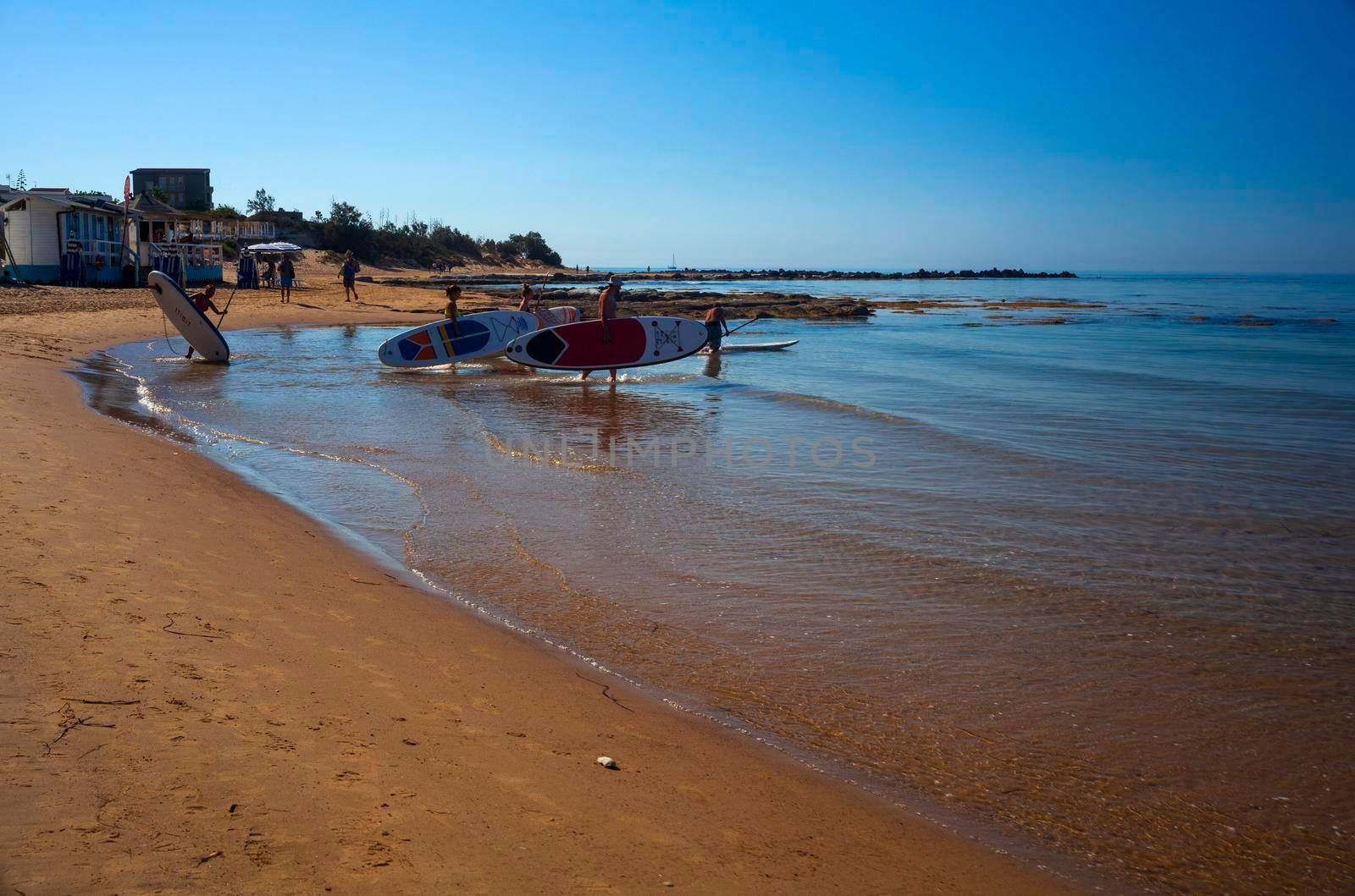 Realmonte, Italy - July 23,: Stand up paddle boarding. Joyful group of friendsare training SUP board in the mediterranean sea on a sunny morning in Realmonte beach on July 23, 2021