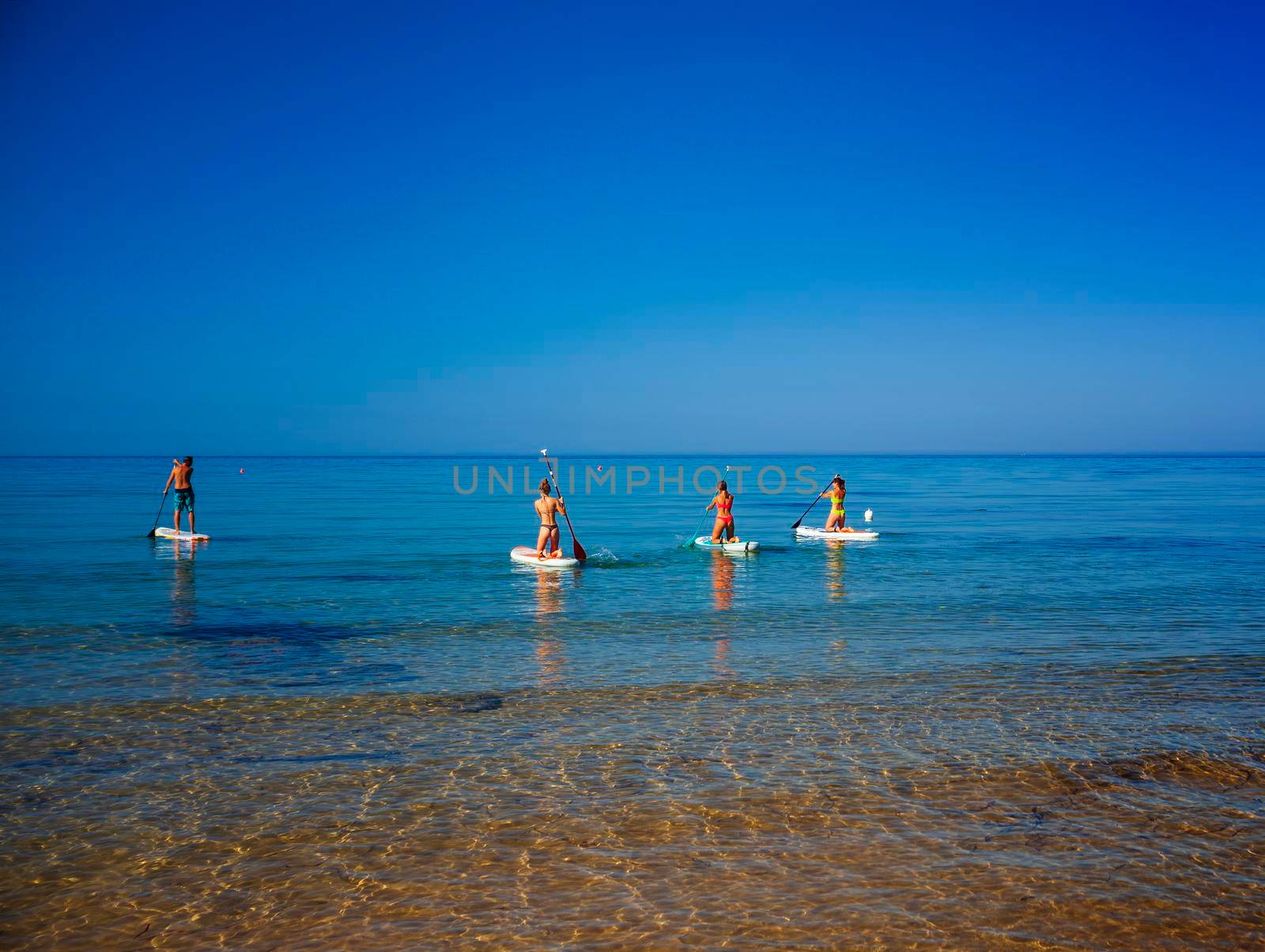 Stand up paddle boarding. Joyful group of friendsare training SUP board in the mediterranean sea on a sunny morning in Realmonte beach by bepsimage