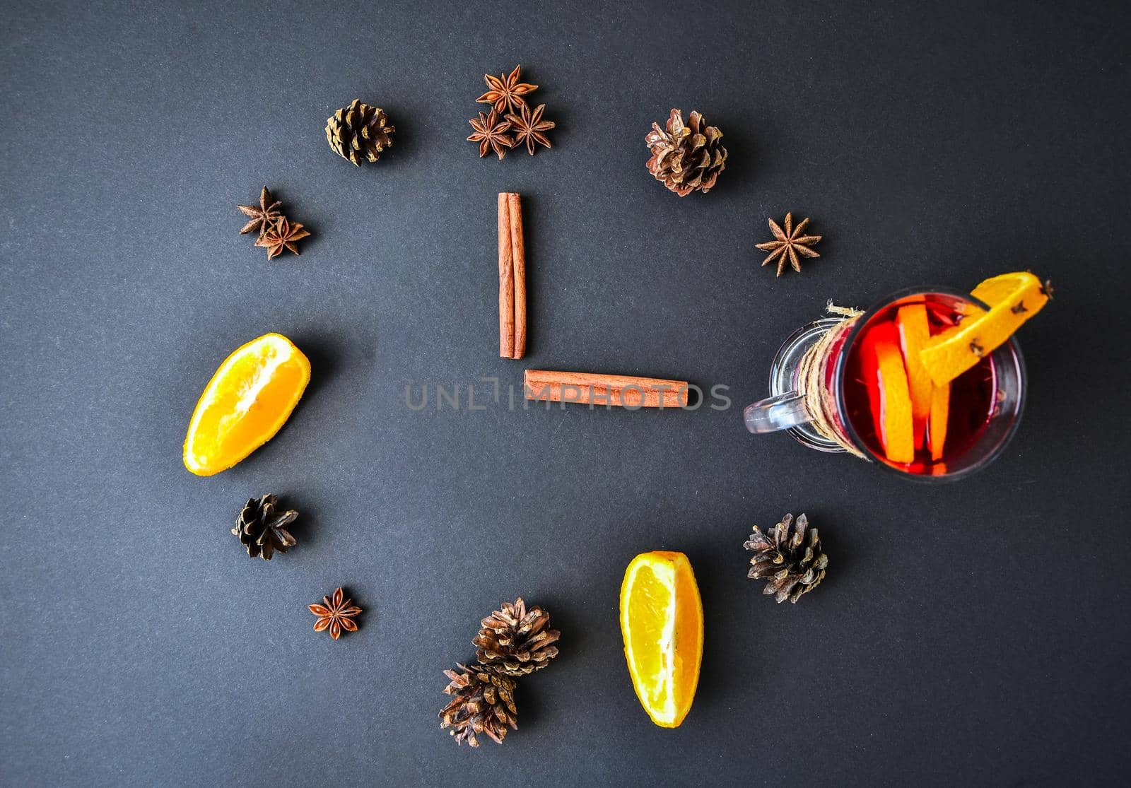 A clock in the form of spice for mulled wine on black background. Cinnamon sticks, anise stars, pine cones, slice of orange. Concept, creative work. Top view by anna_stasiia