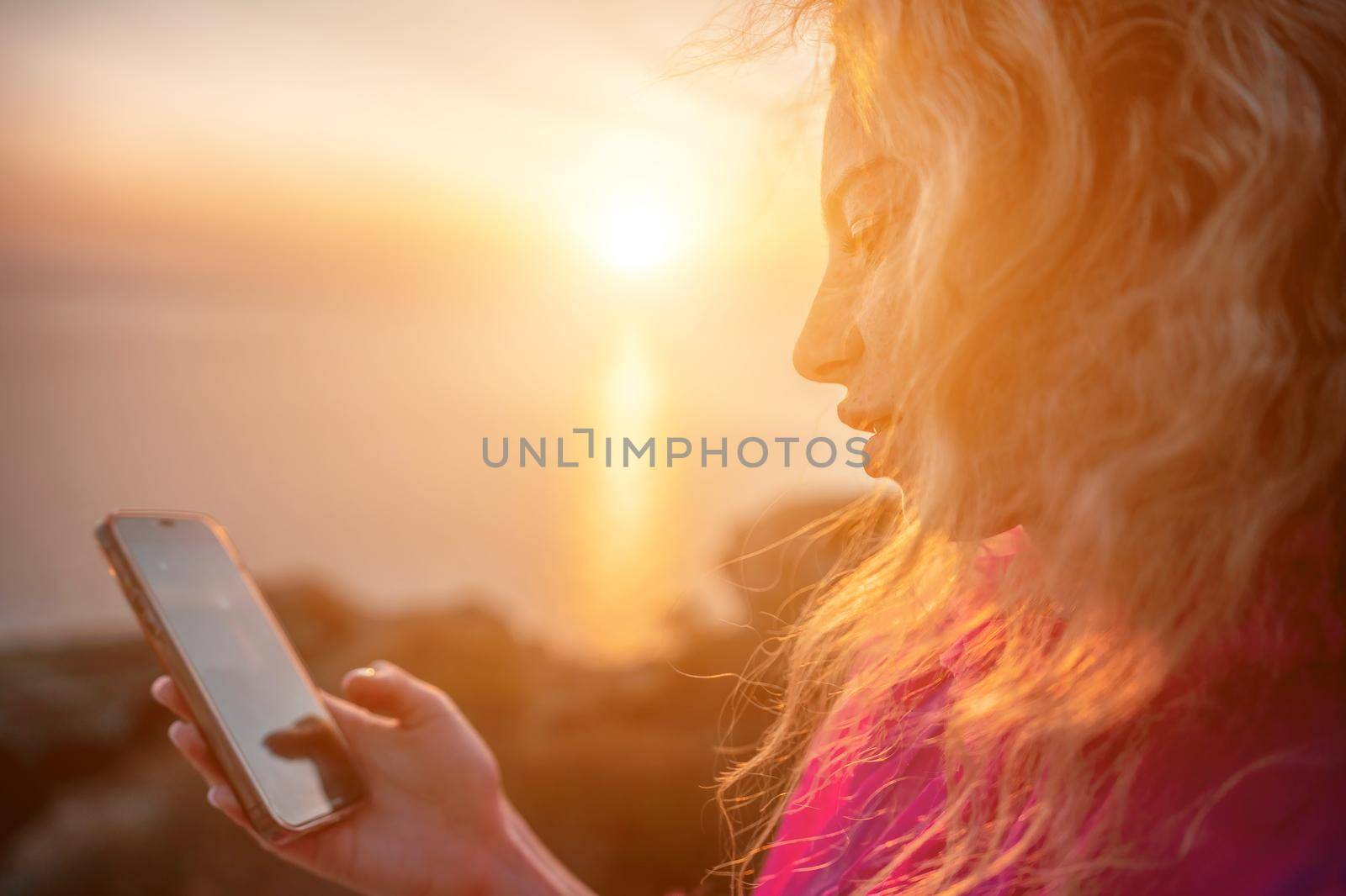 Side view a Young beautiful sensual woman in a red long dress posing on a volcanic rock high above the sea during sunset. Girl on the nature on overcast sky background. Fashion photo