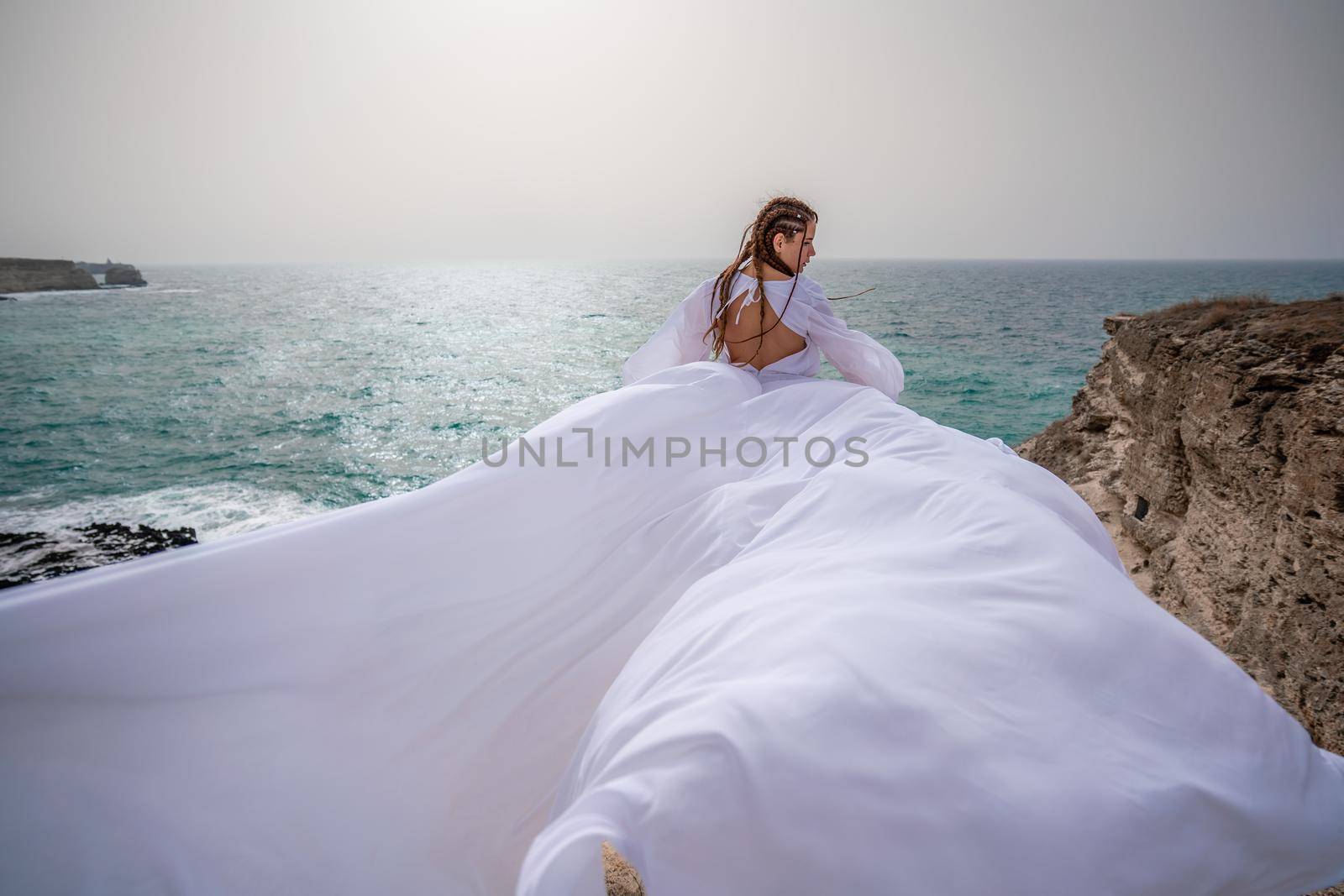 Happy freedom woman on the beach enjoying and posing in white dress. Rear view of a girl in a fluttering white dress in the wind. Holidays, holidays at sea. by Matiunina