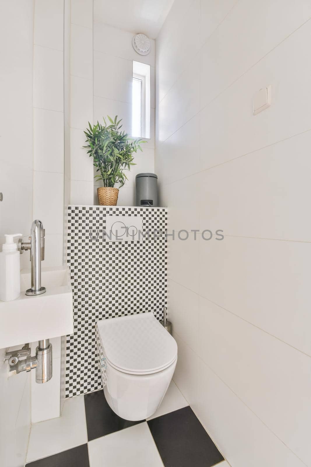 Modern flush toilet and ceramic sink installed on white tiled walls near mirror and towel in small restroom at home