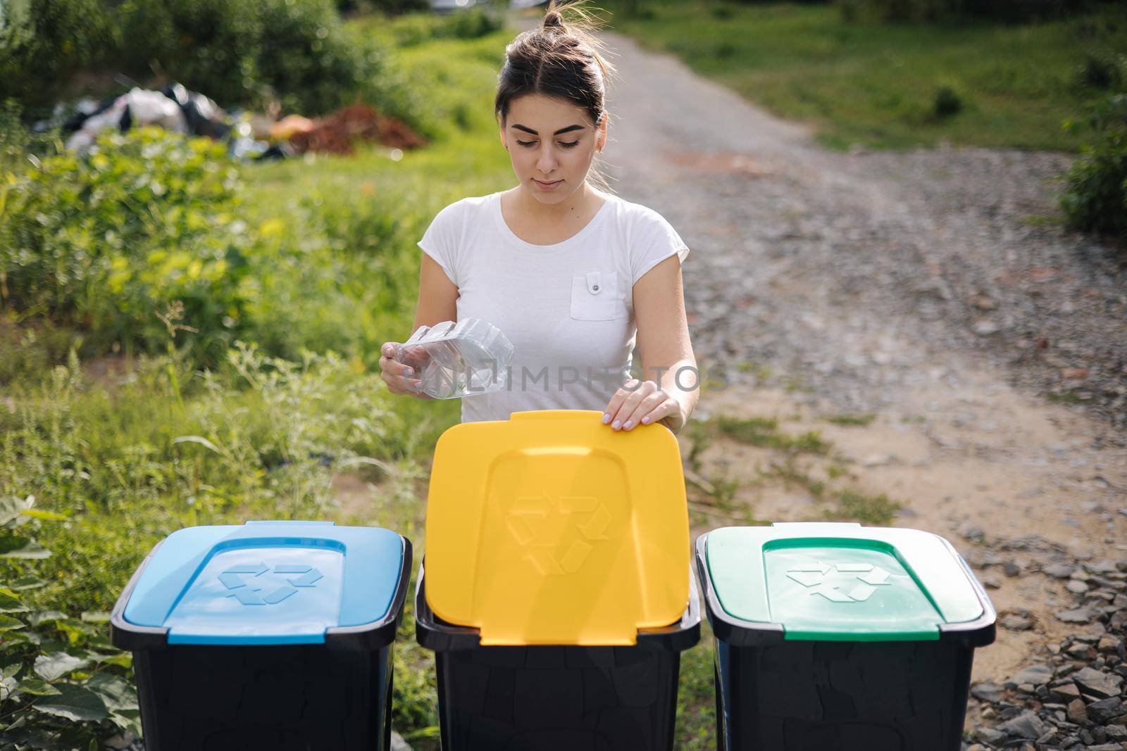 Front view of female throwing out in recycling bin clean empty plastic container. Different colour of recycling bins.