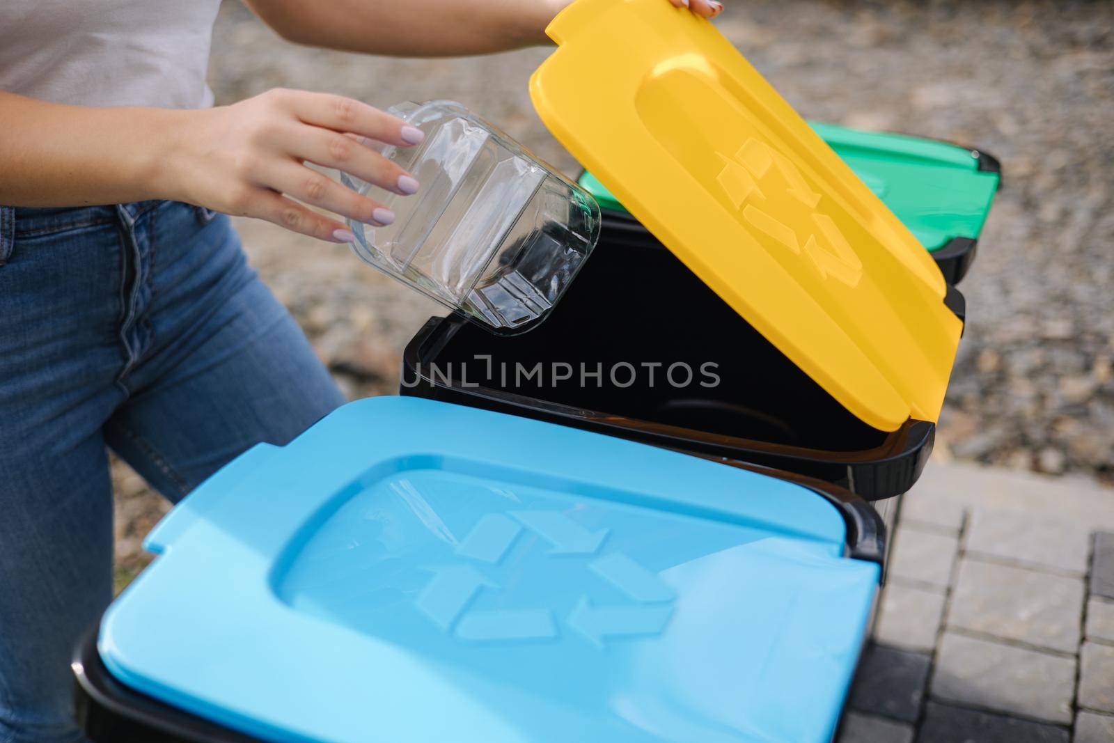 Close of female throwing out in recycling bin clean empty plastic container. Different colour of recycling bins.