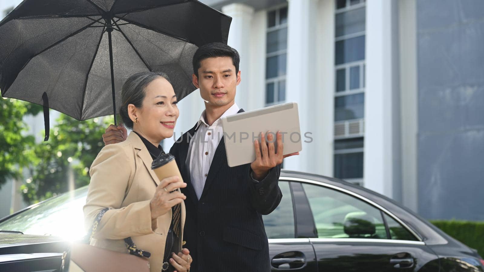 Attractive senior businesswoman having a discussion with her assistant while standing at modern office district.