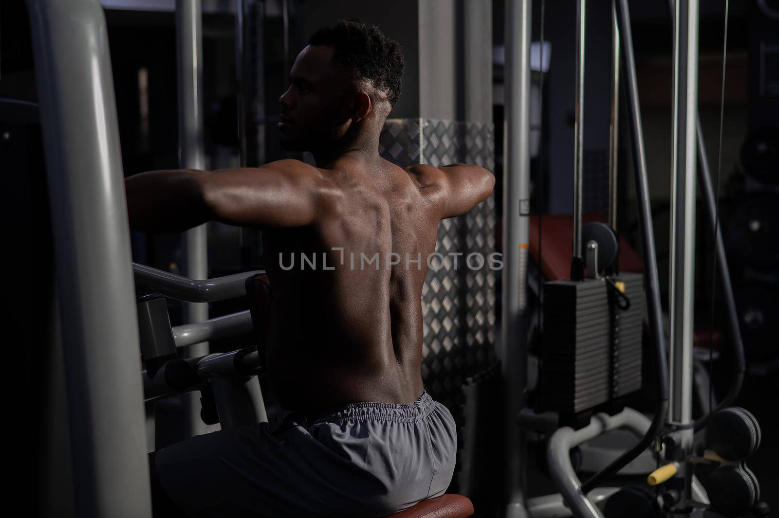 Shirtless african american man doing back exercises on a machine in the gym