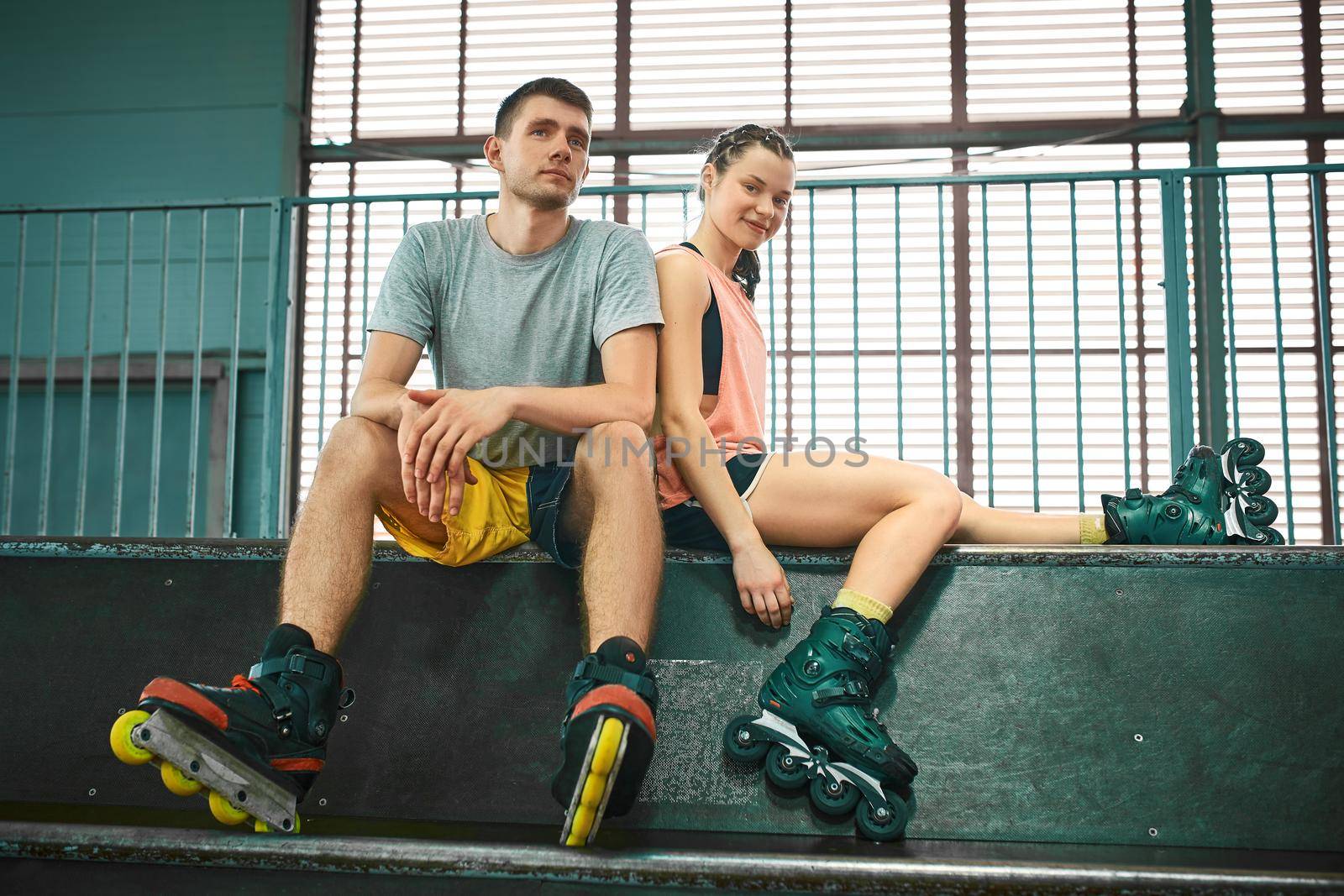 Young man and woman having fun on roller skates in skate park. Extreme sport competition. Indoors skate park equipment. Hobby